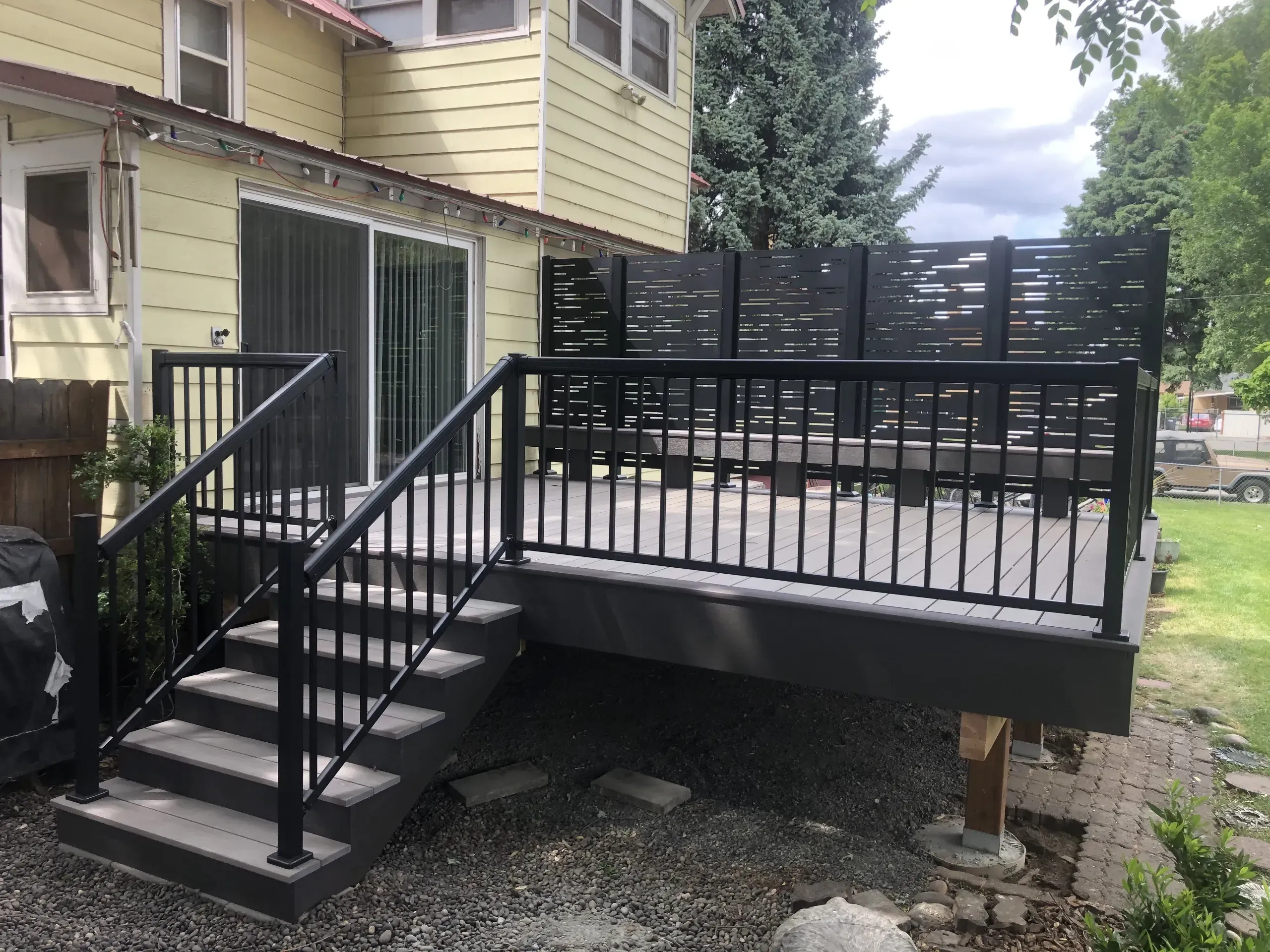 A grey composite deck with black aluminium railing and tall louvred privacy screens along the far edge.