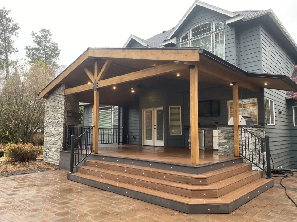 Covered deck with a cedar gable, stone columns, outdoor kitchen and wide composite steps with recessed step lights