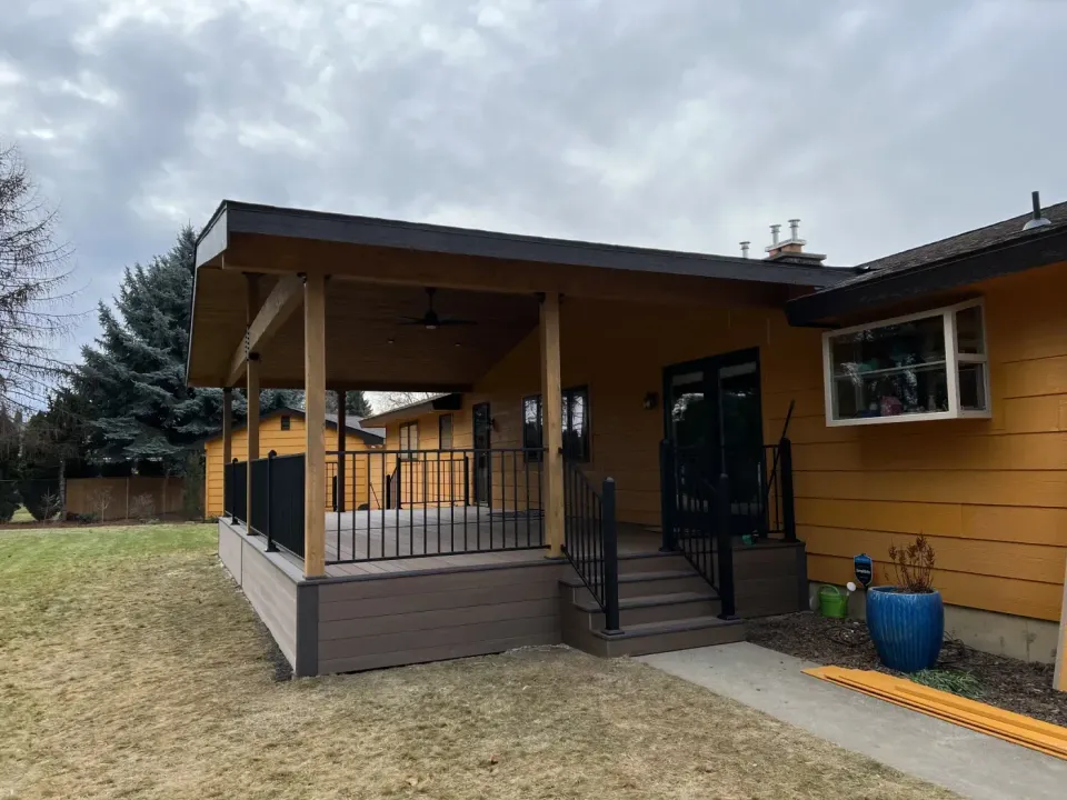 Covered deck with cedar posts, a ceiling fan and black aluminum railing, beside a lawn
