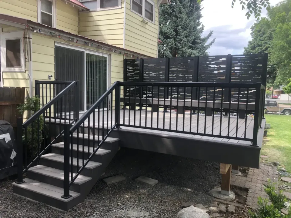 Grey composite deck with a louvered black privacy screen, black aluminum railing and matching stairs