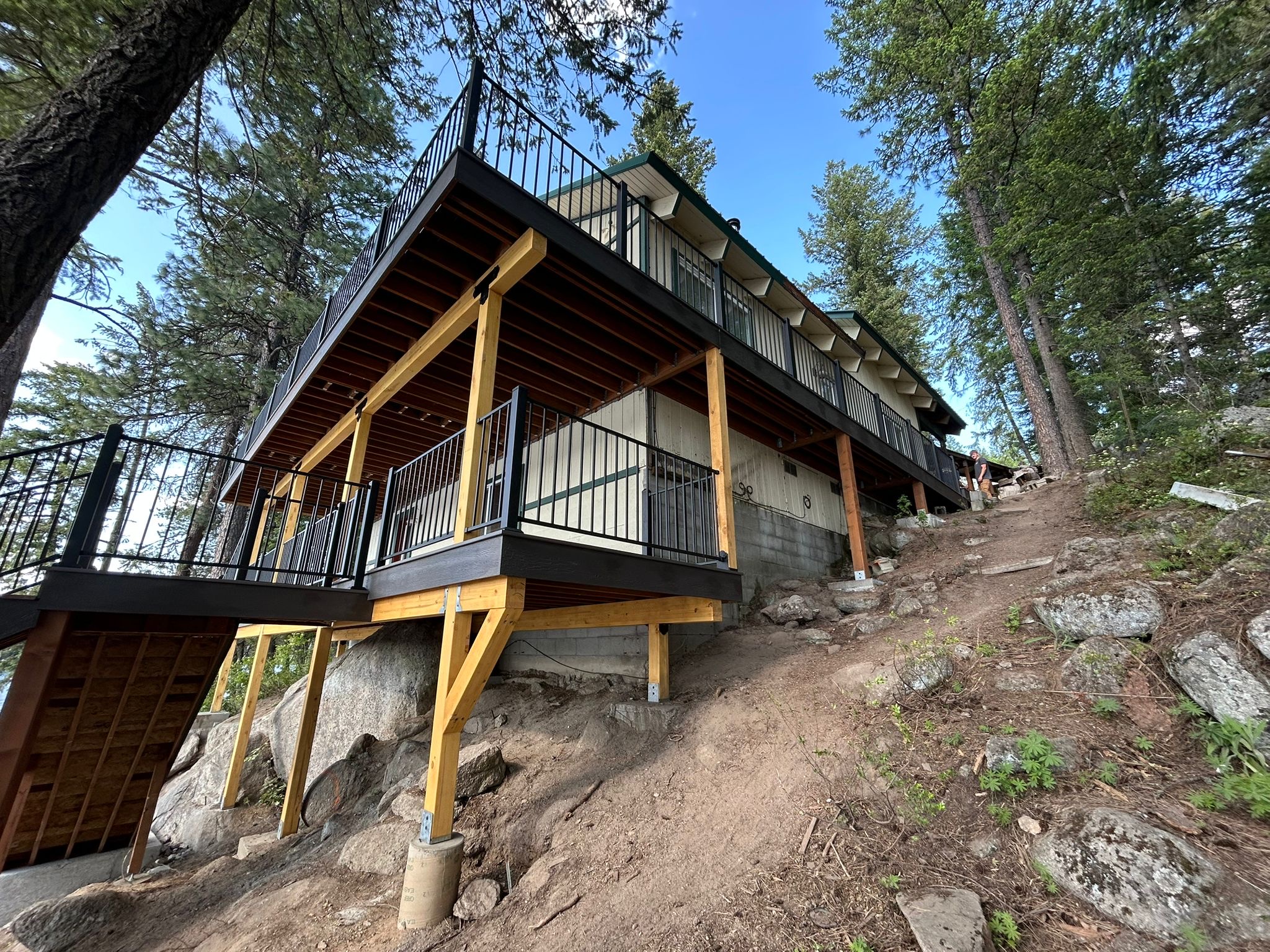 Multi-level deck built on a steep rocky hillside with cedar-wrapped posts and black railing