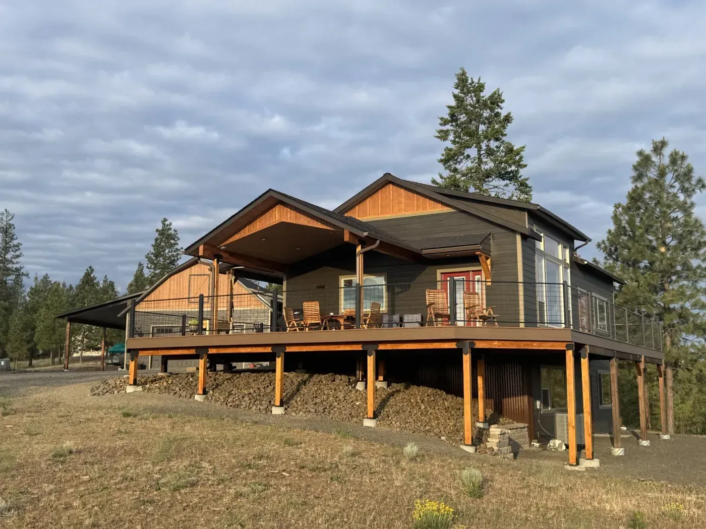 Large wraparound deck raised on cedar posts with cable railing, on an acreage property at golden hour