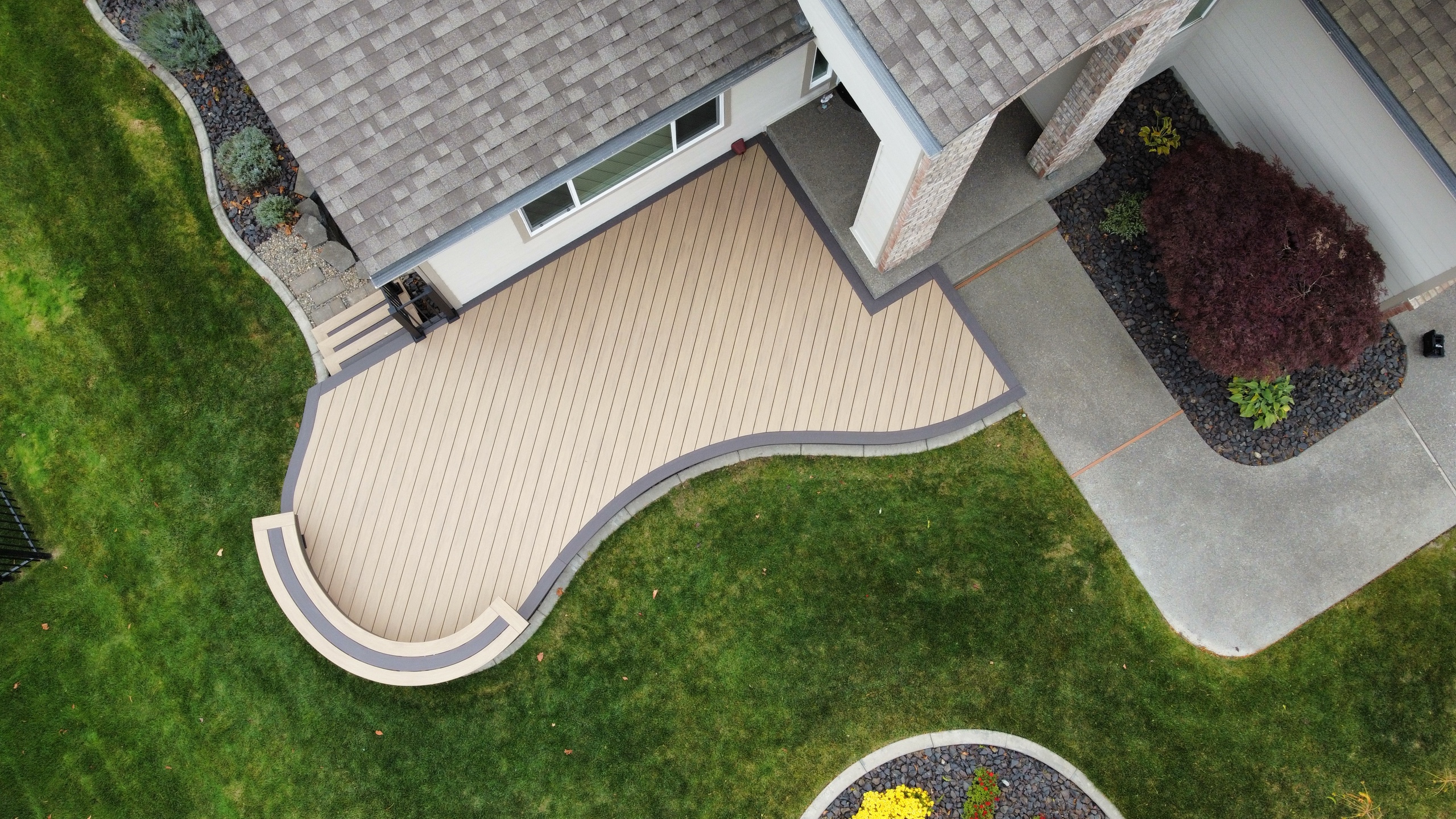 Aerial of curved beige composite deck wrapping from a house corner with lawn and landscaping