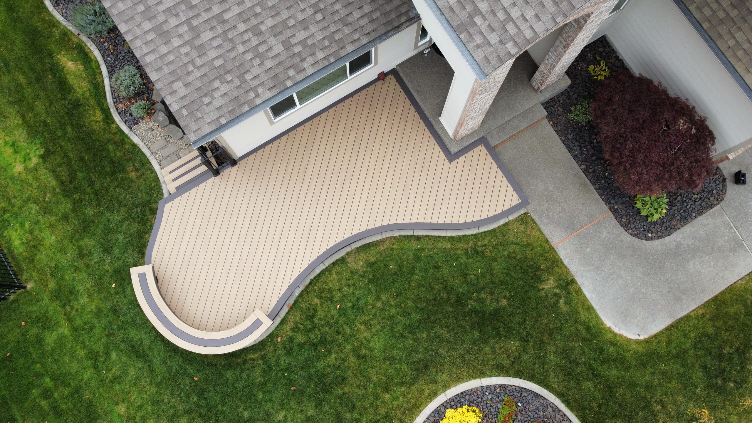 Aerial of curved beige composite deck wrapping from a house corner with lawn and landscaping