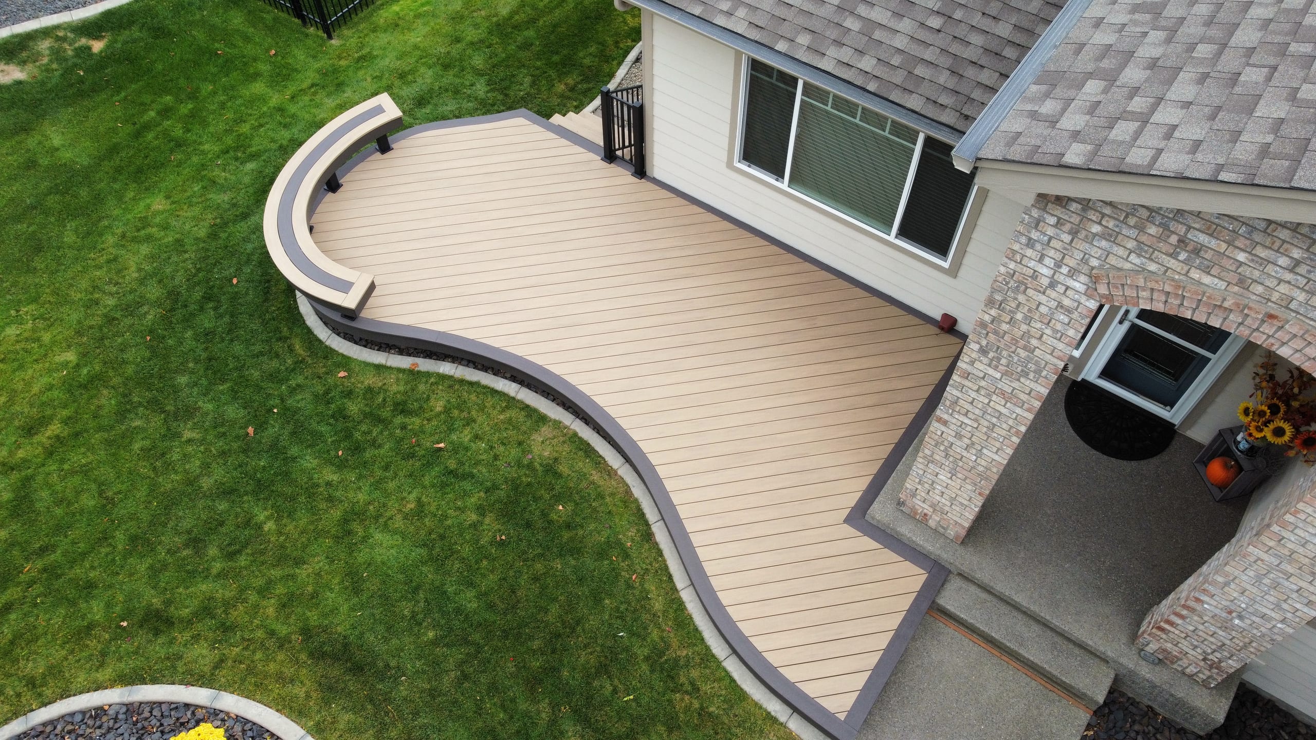 Aerial view of a curved tan deck with dark border and bench beside a brick entry