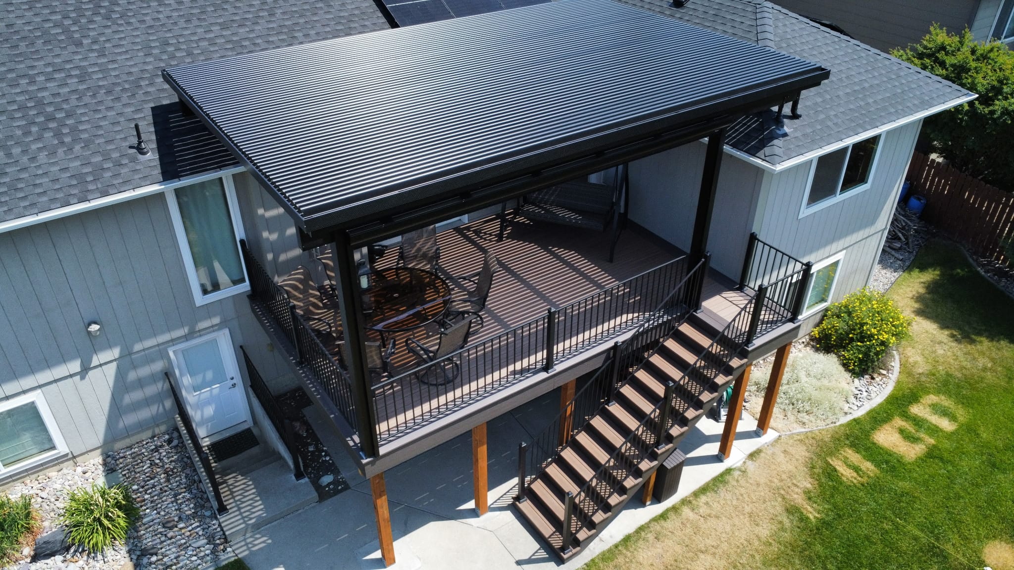 Aerial view of dark louvered pergola roof over an elevated composite deck with black metal railing and stairs