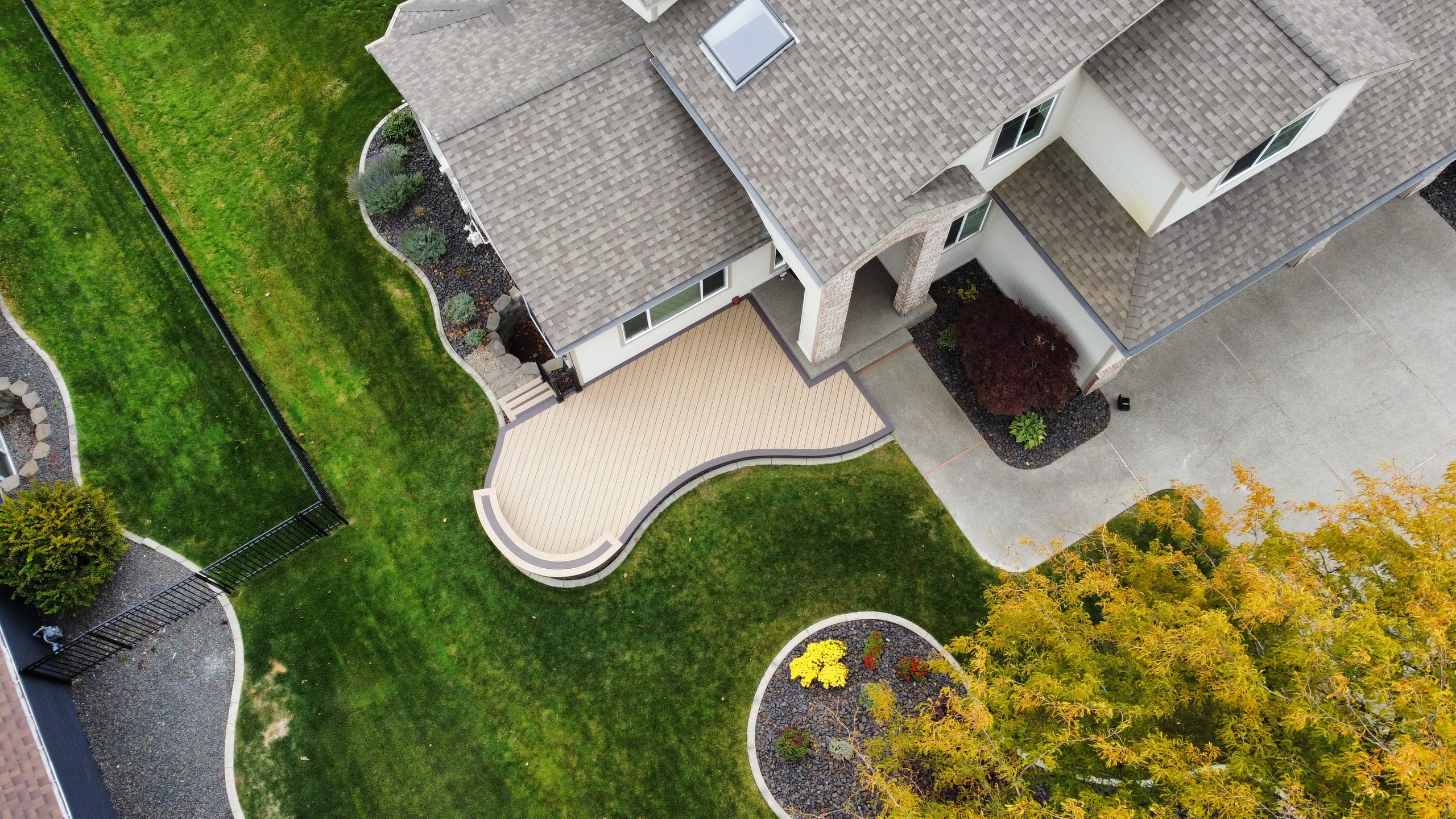 Aerial of house front with small curved beige composite deck and walkway, lawn and landscaping