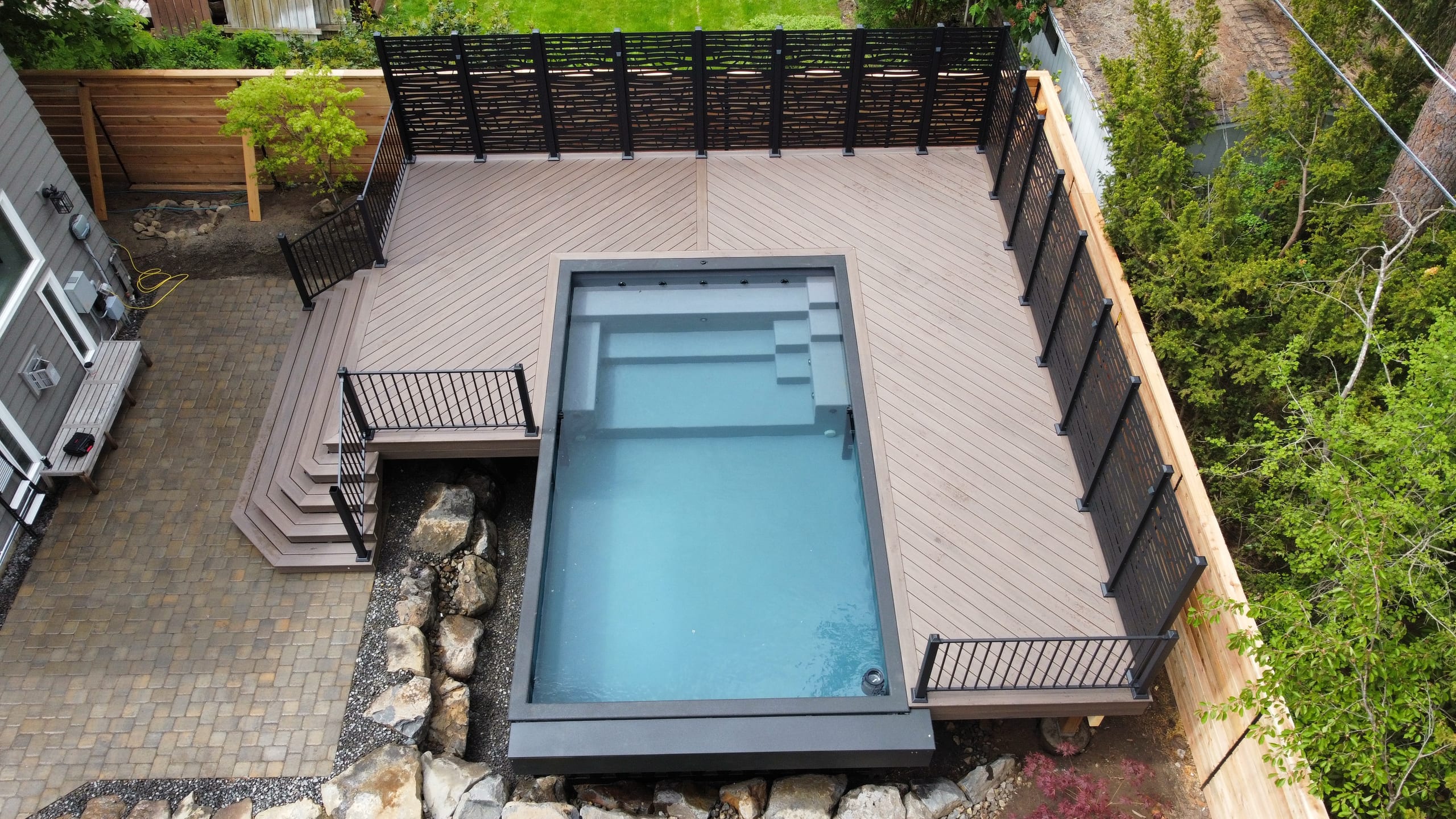 Aerial overhead of pool deck with herringbone composite pattern, black screen, wood fence and steps