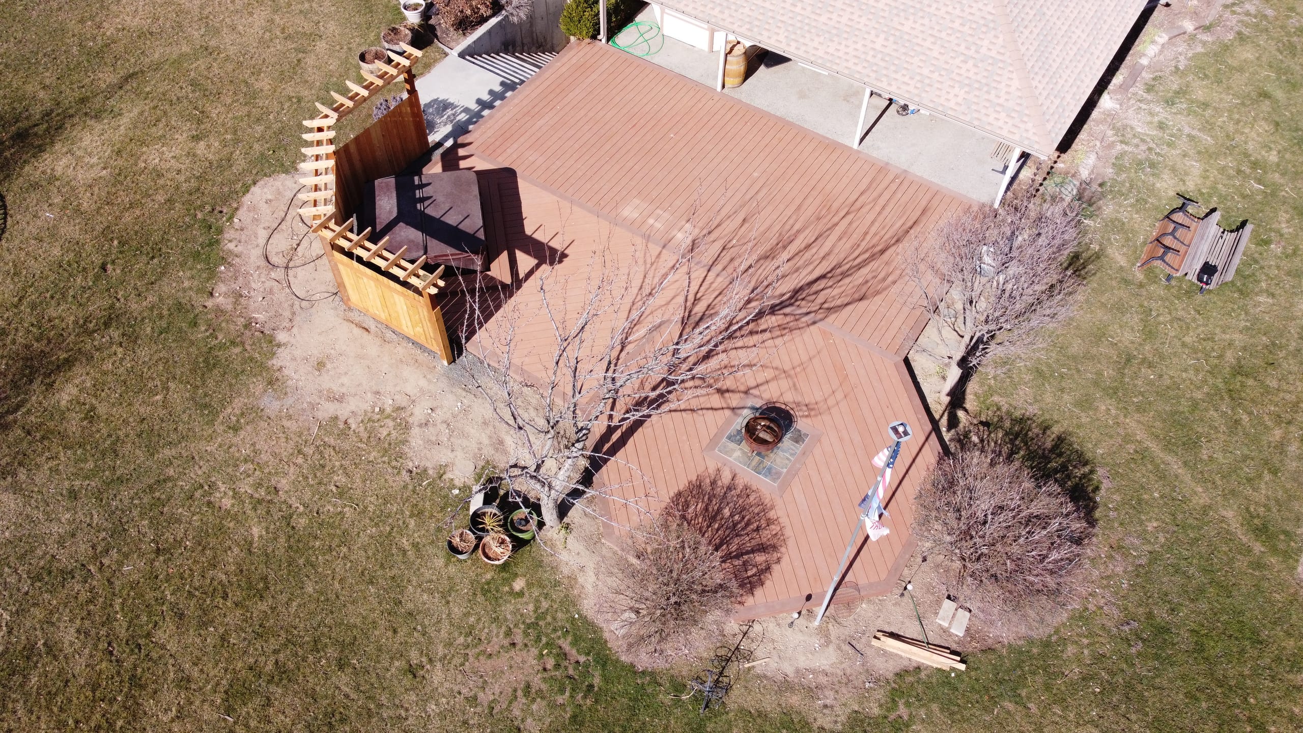 Aerial of reddish composite deck with cedar corner screen, fire pit and flagpole beside house