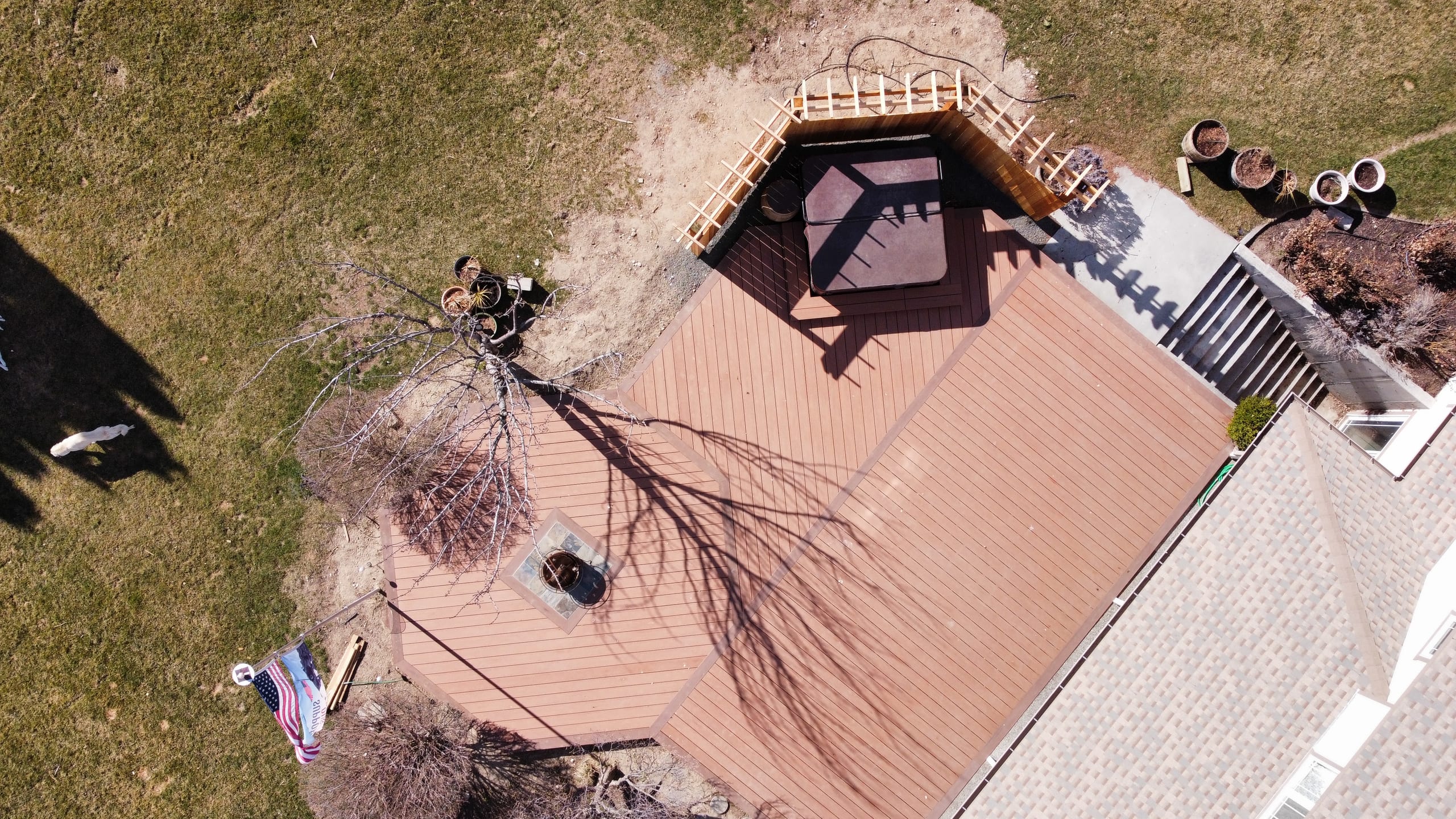 Aerial of reddish composite deck with hexagonal cedar pergola hot tub corner, fire pit and stairs to house