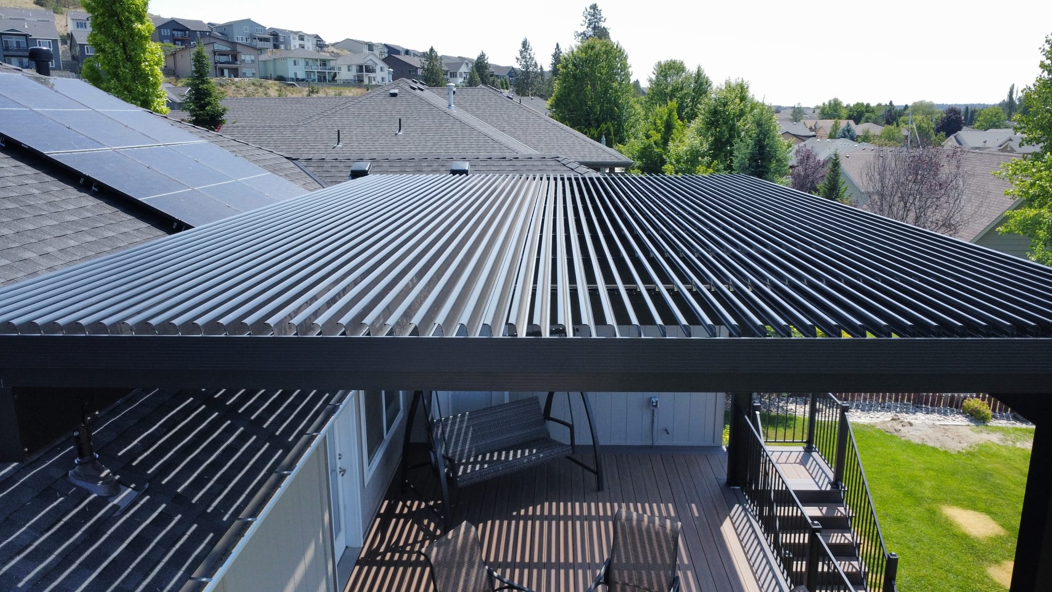 Aerial top-down view of a black louvered roof over an elevated deck with outdoor seating and stairs