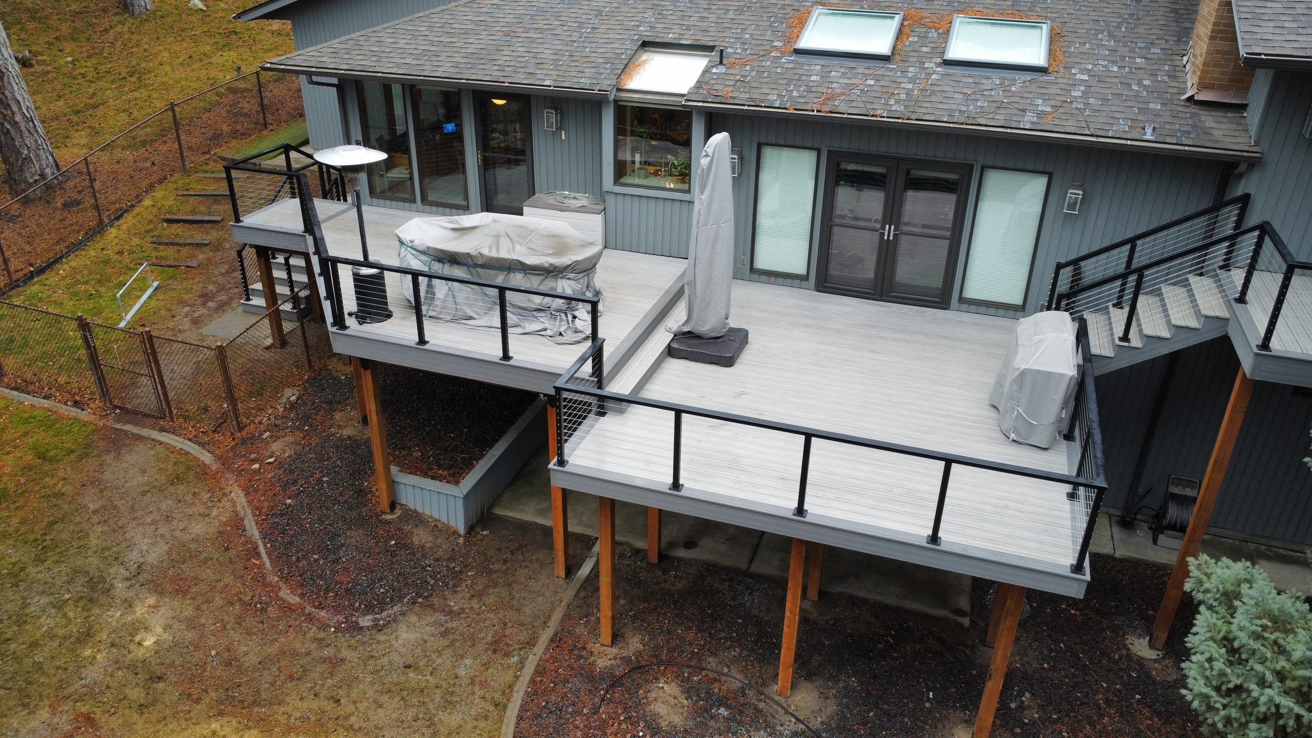 Aerial view of two-level gray composite deck on cedar posts with black railing, covered hot tub