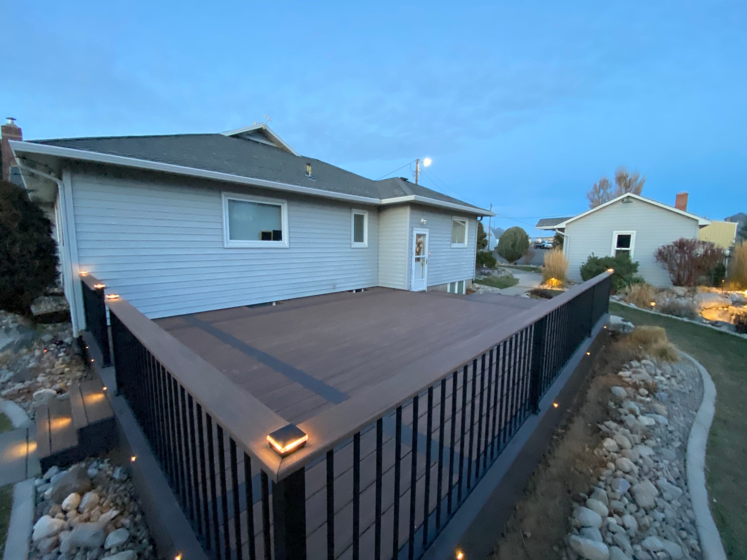 Angled view along black picket railing with lit post caps on brown composite deck at twilight