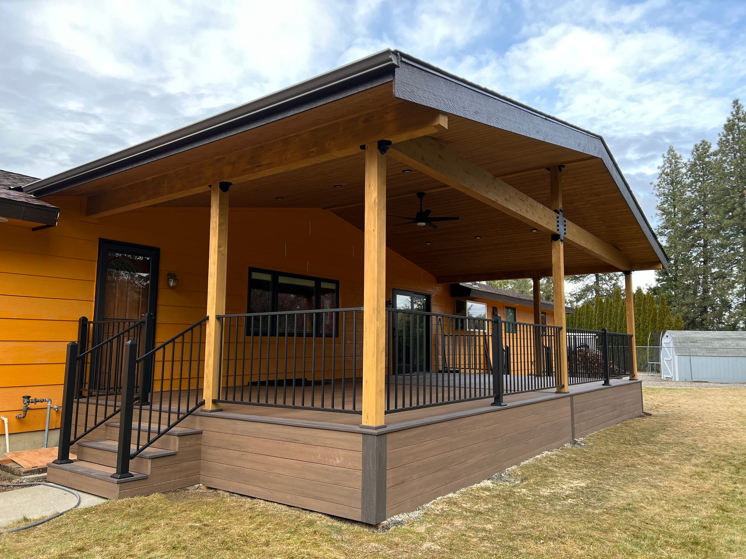 Angled view of covered deck on orange house with cedar posts, hip-gable roof, black railing and brown composite skirt