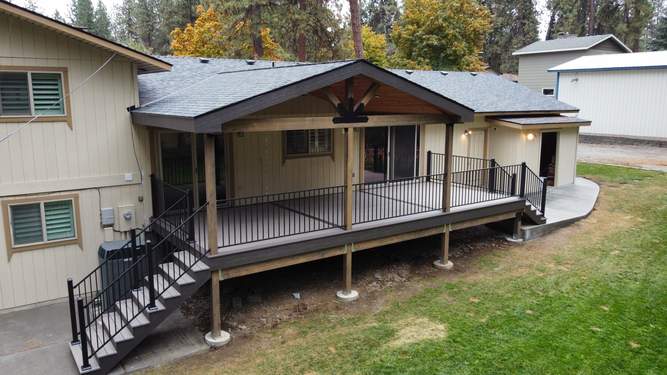 Angled view of elevated gray deck with gable cover, black metal railing and black stair run, lawn in front