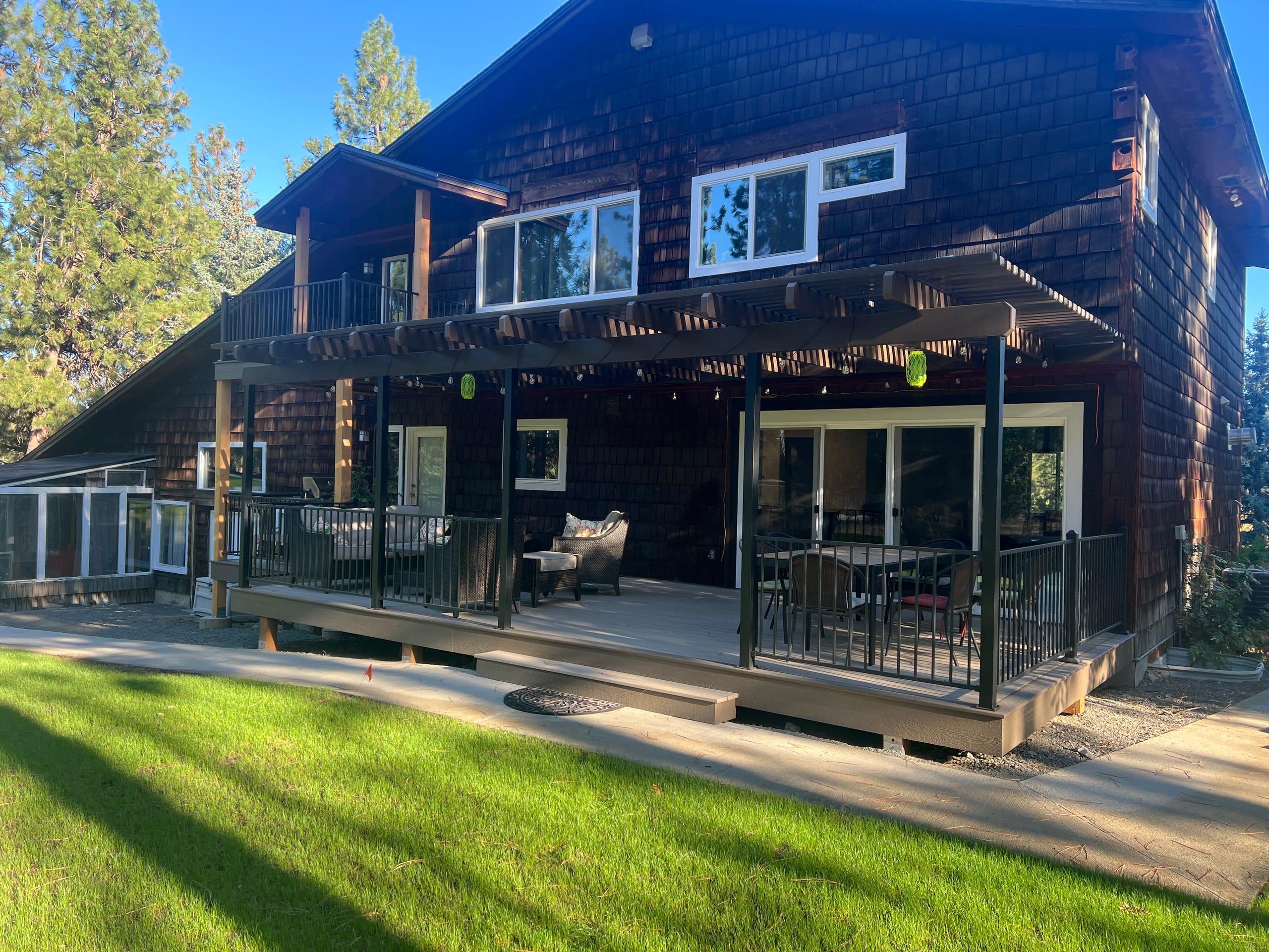Backyard composite deck with black railing and a pergola attached to a dark shingled home, lawn foreground