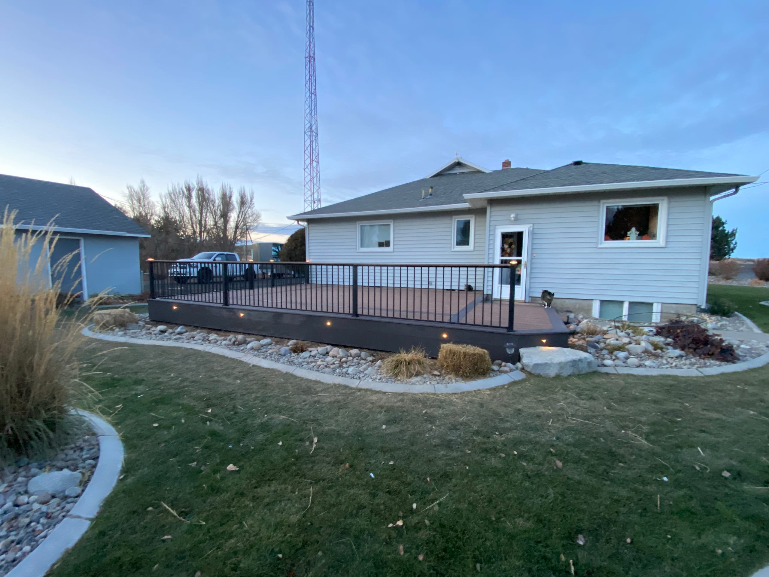 Backyard at twilight with low composite deck with black railing and fascia lights along a pale house