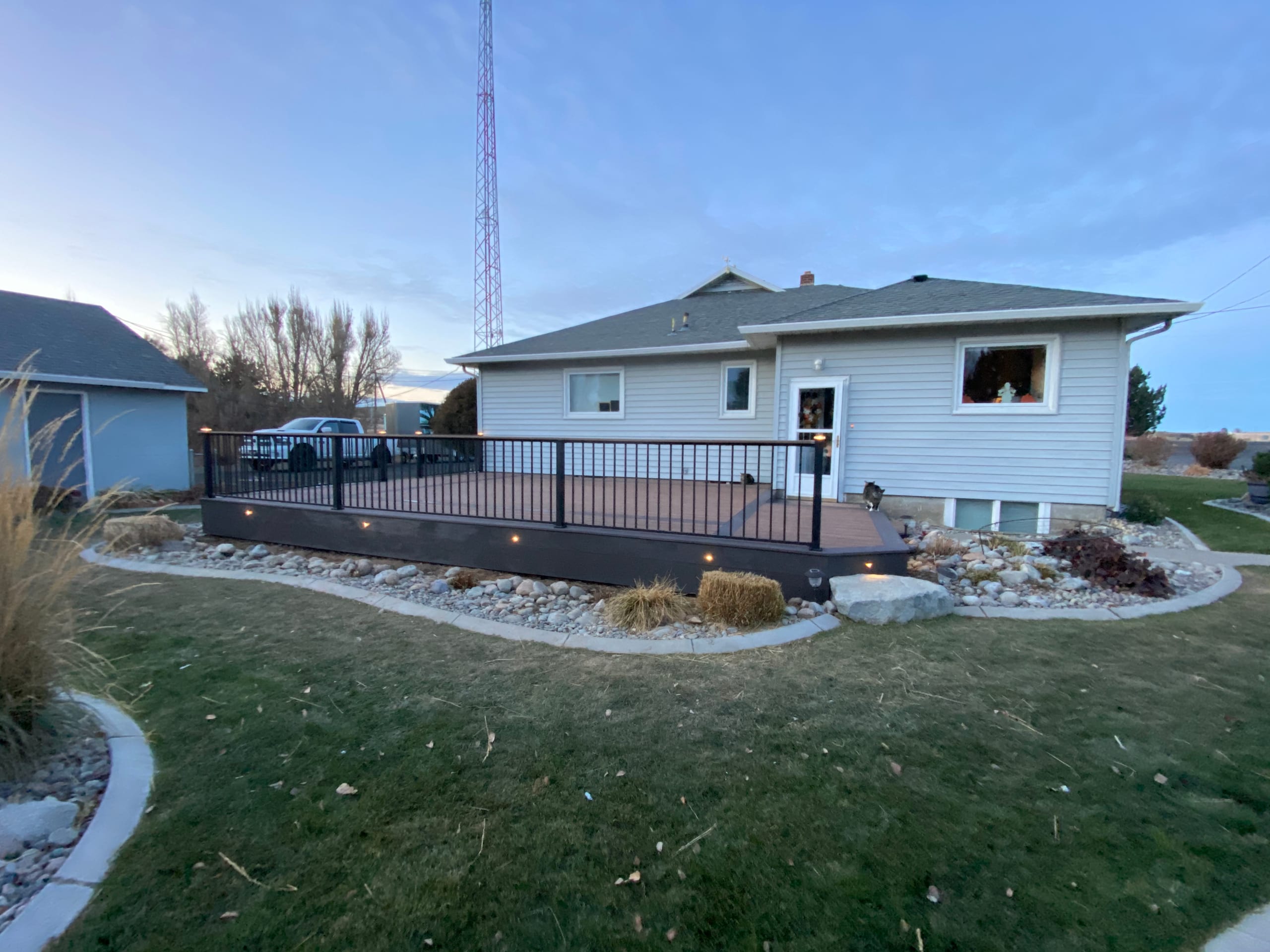 Backyard at twilight with low composite deck with black railing and fascia lights along a pale house