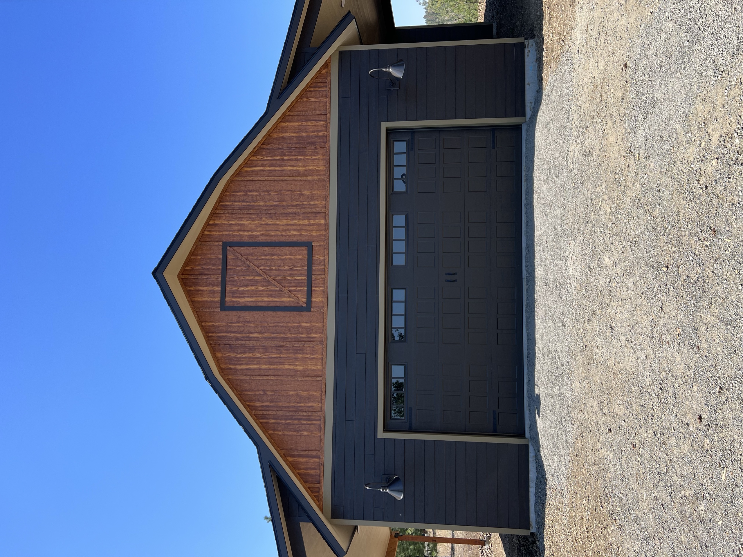 Barn-style garage with a cedar board-and-batten gable, dark siding and a two-car door on a gravel apron