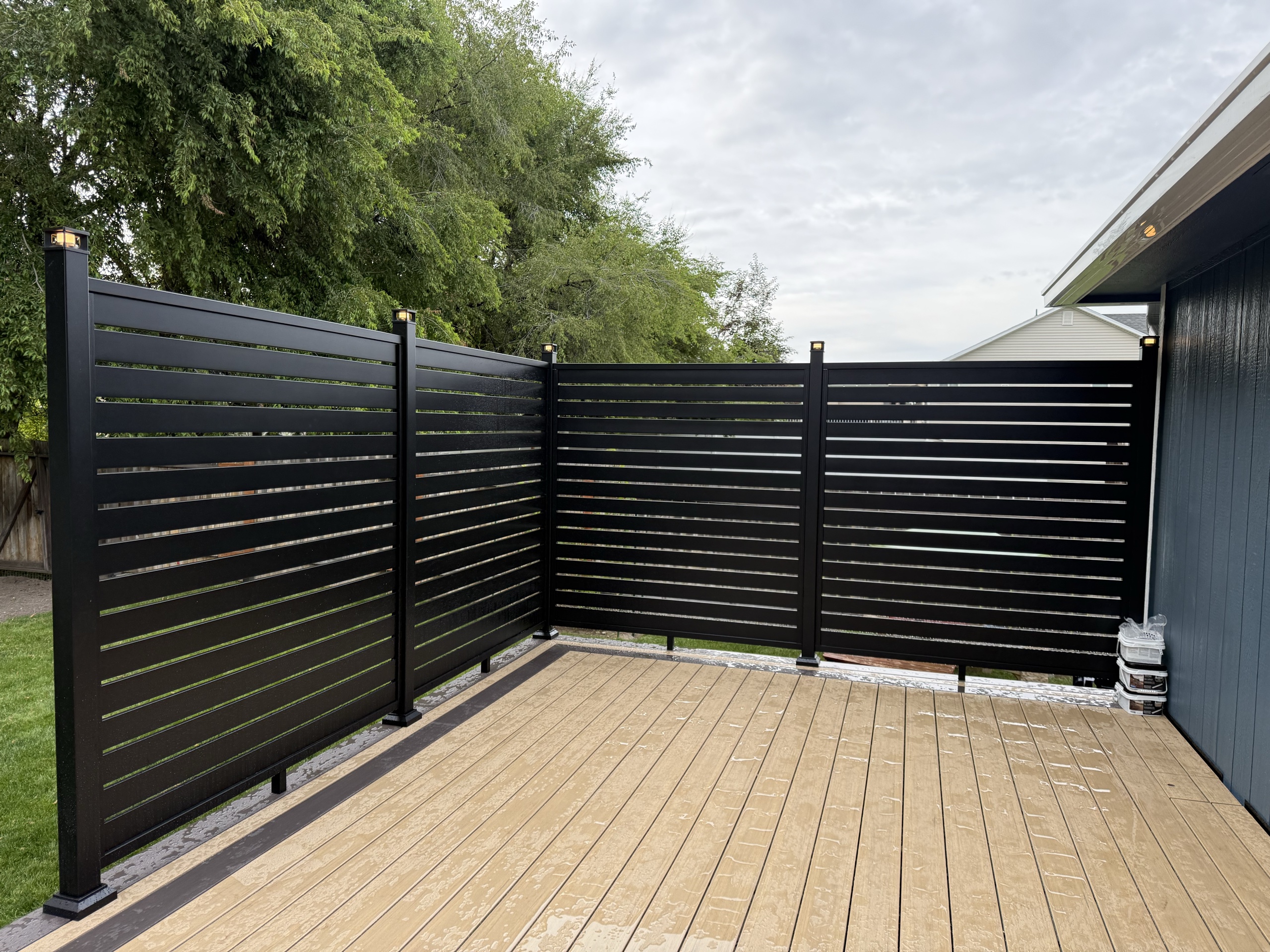 Black horizontal-slat aluminum privacy screen in an L around a tan composite deck