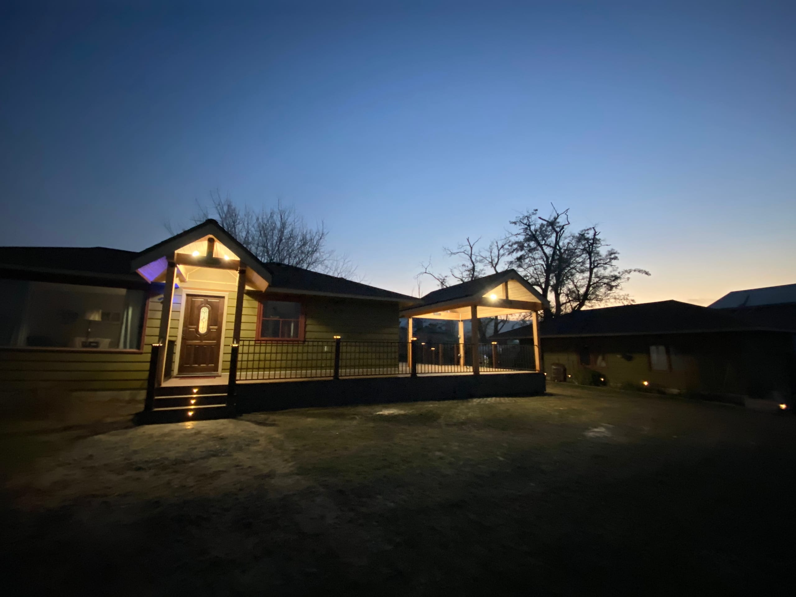 Blue-hour view of front entry porch with accent lighting and adjacent gabled covered deck with black railing