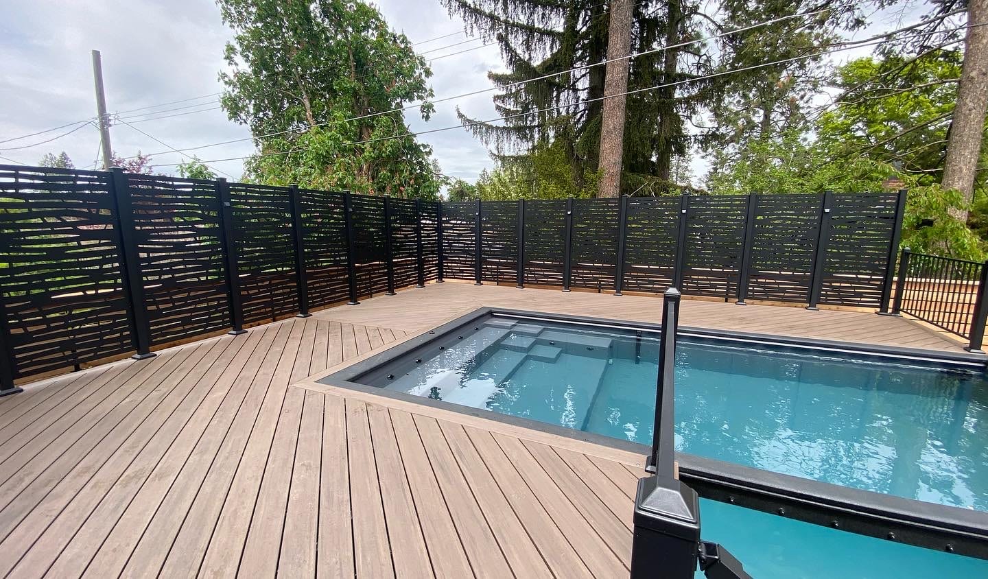 Brown composite deck around in-ground pool with black louvered screen and railing post