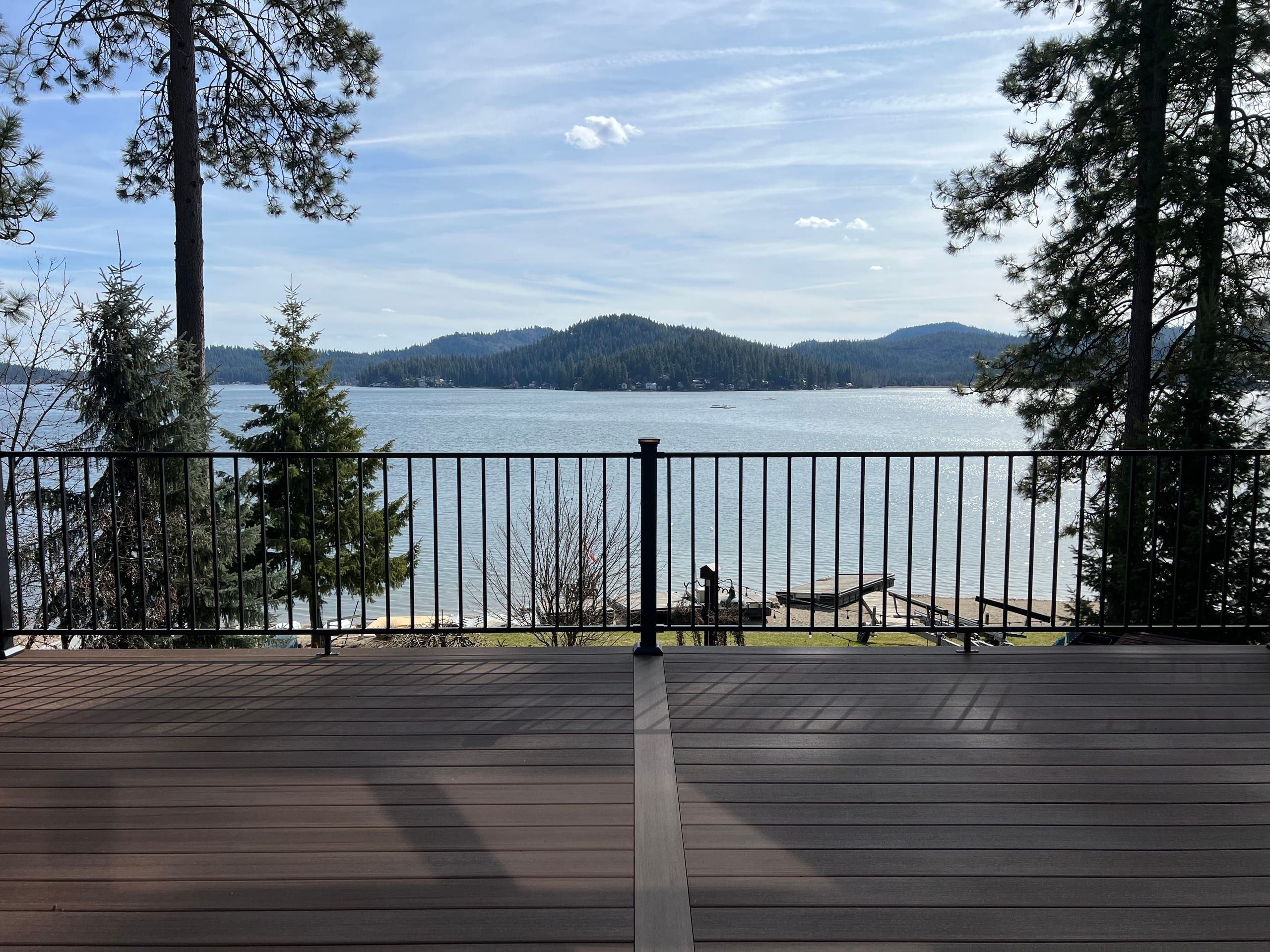 Brown composite deck with black picket railing and a wide lake and mountain view under blue sky