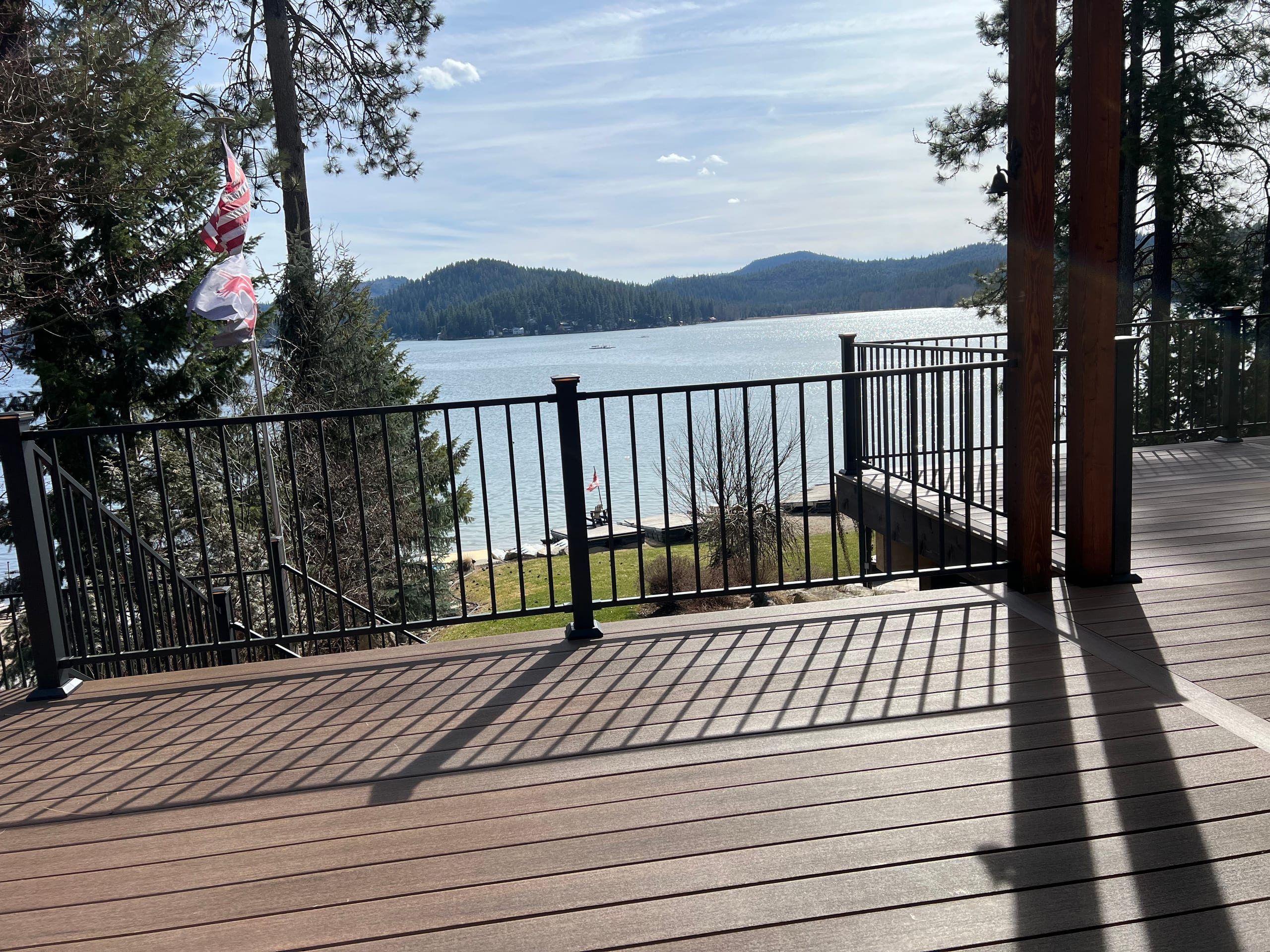 Brown composite deck with black picket railing and wood posts looking over a blue lake and hills with US flag