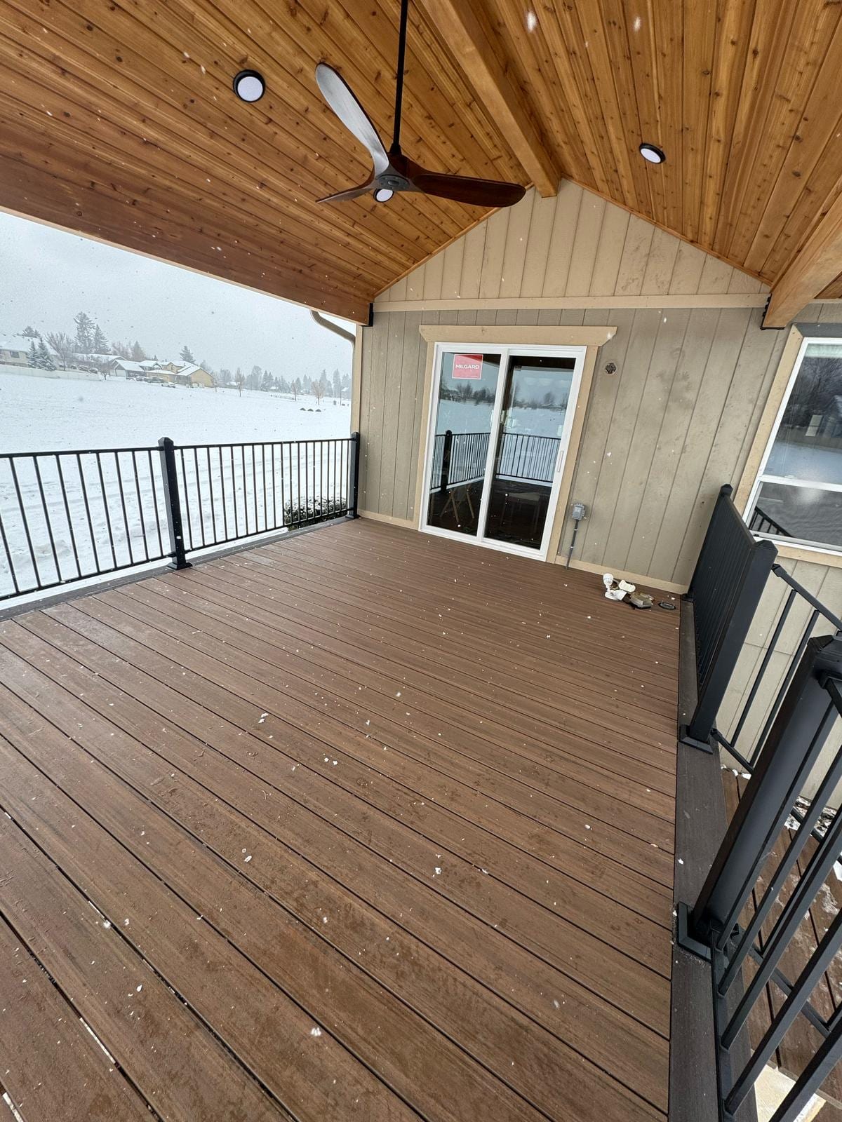 Brown composite deck under a covered porch with wood tongue-and-groove ceiling, ceiling fan and lake view
