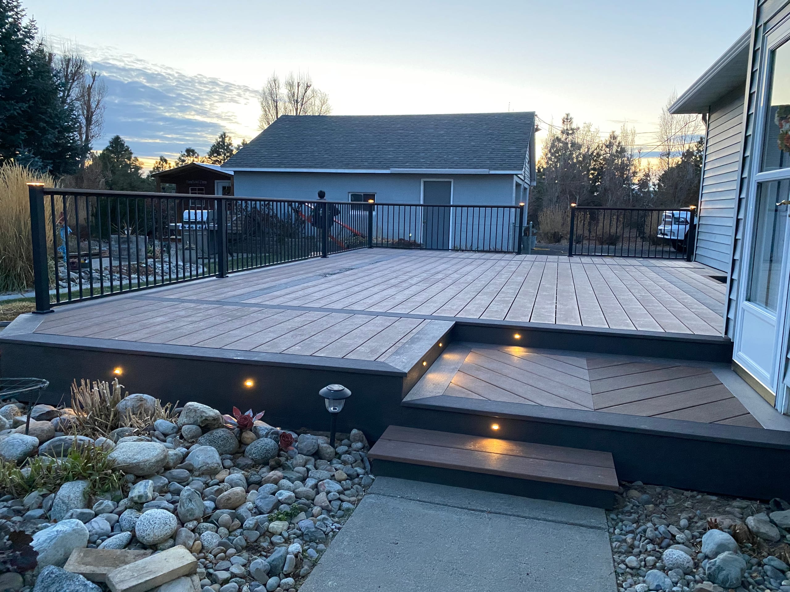 Brown composite deck with picture-frame border, lit step down to a landing and black railing