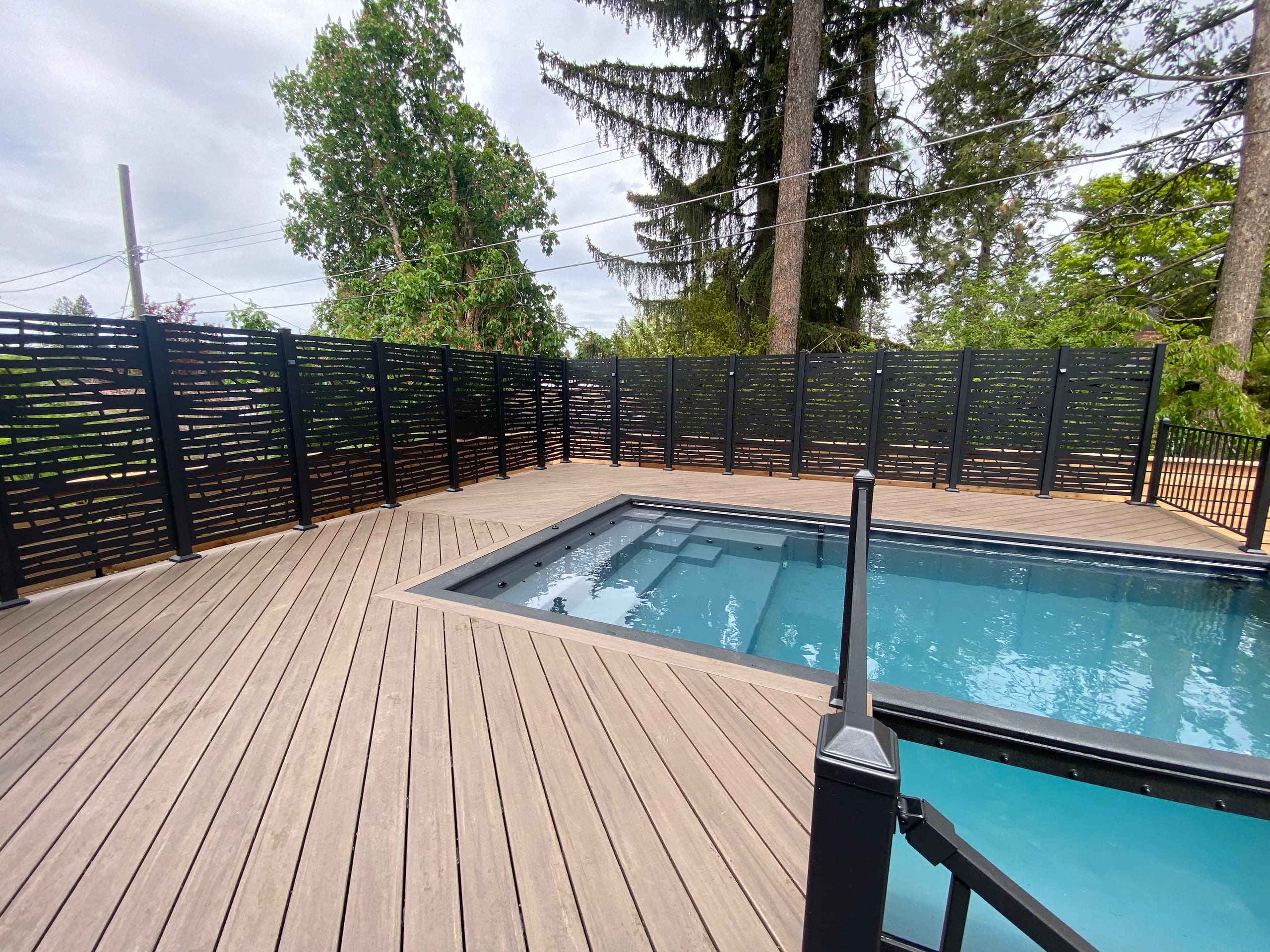 Brown composite deck surrounding an in-ground plunge pool with black louvered privacy screen and railing