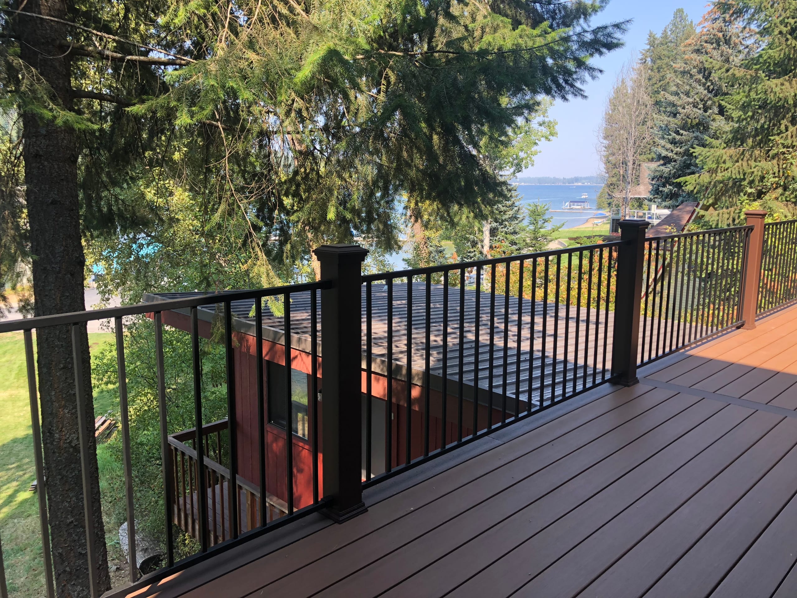 Brown decking with black metal railing looking through trees toward a lake