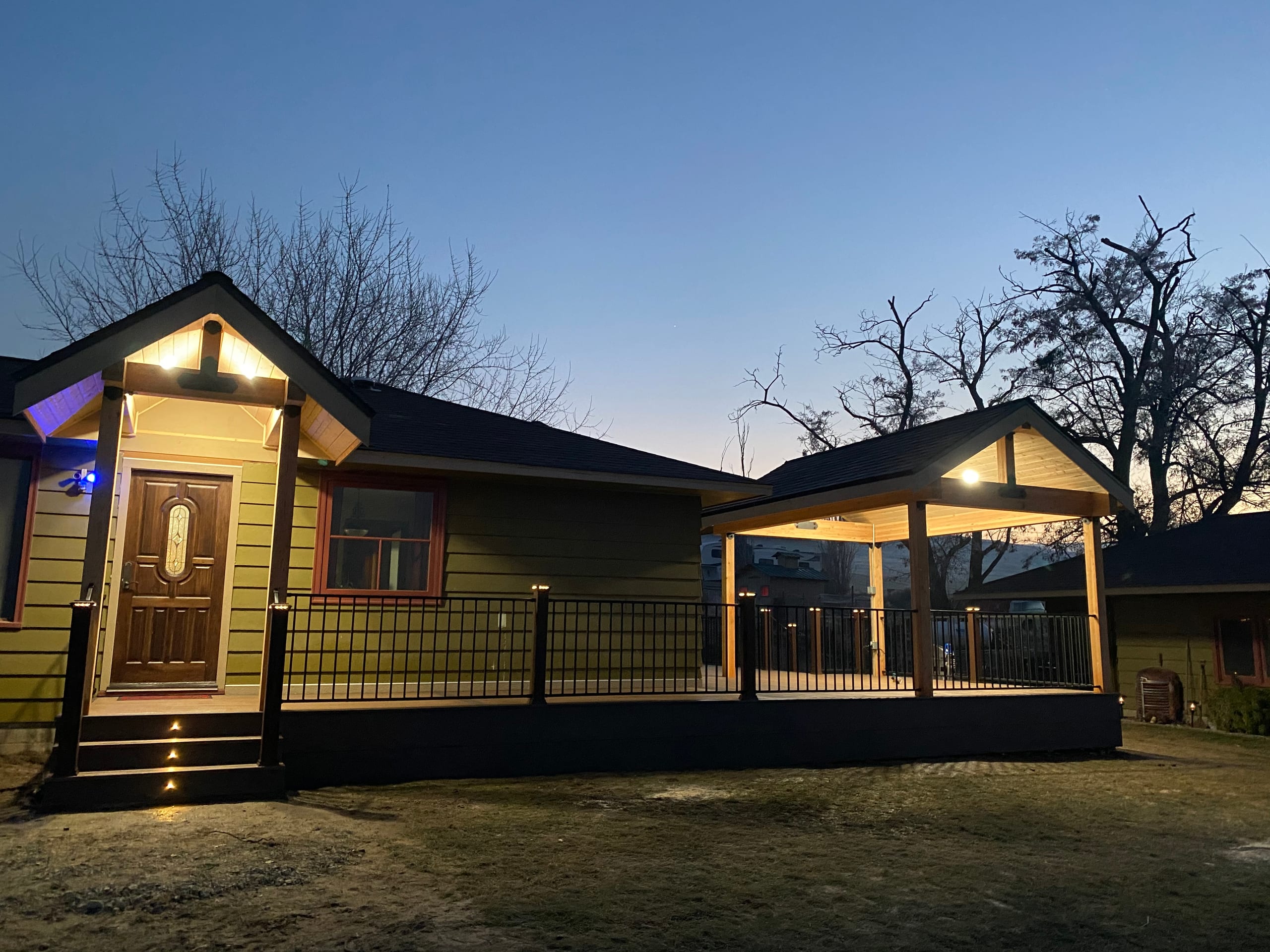 Close dusk view of lit entry porch with ornate door and adjacent gabled covered deck with black picket railing