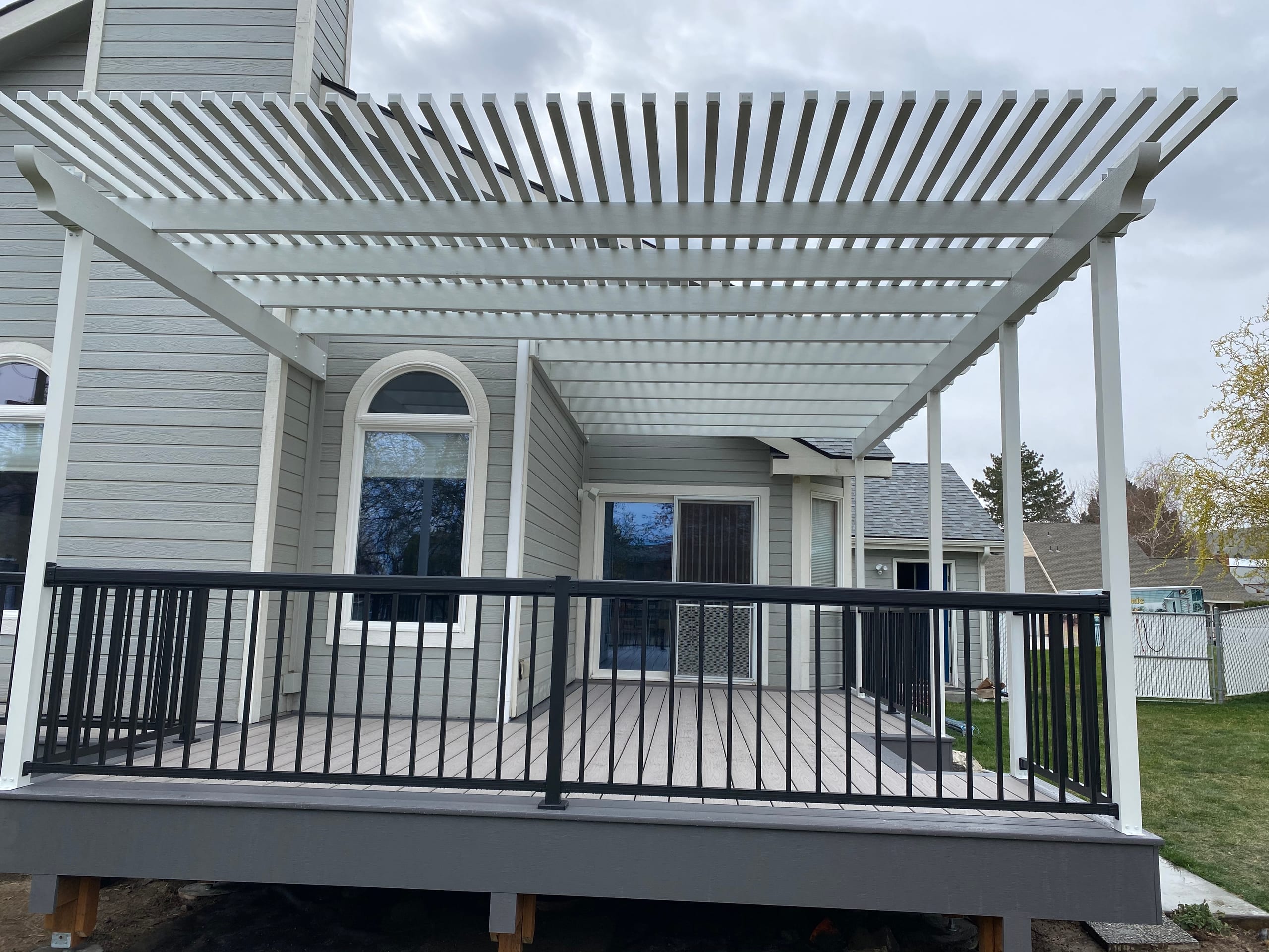 Close view of white louvered aluminum pergola over gray composite deck with black picket railing and dark fascia