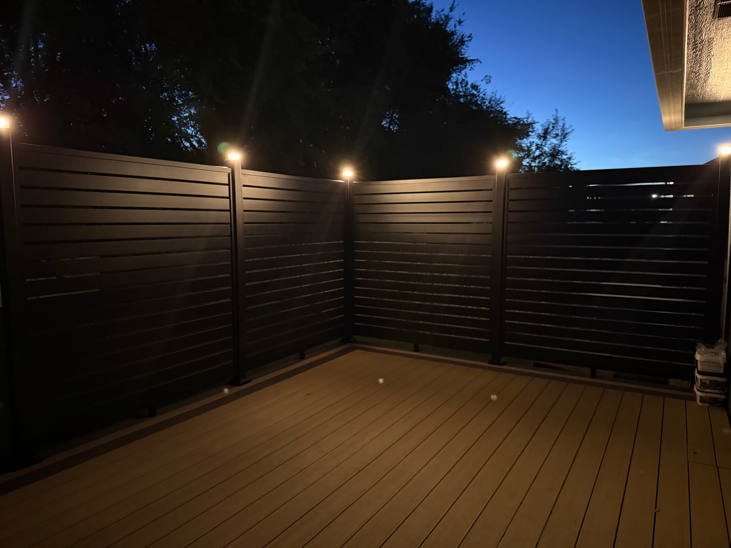 Composite deck corner at dusk with dark slat privacy walls and post-cap lights