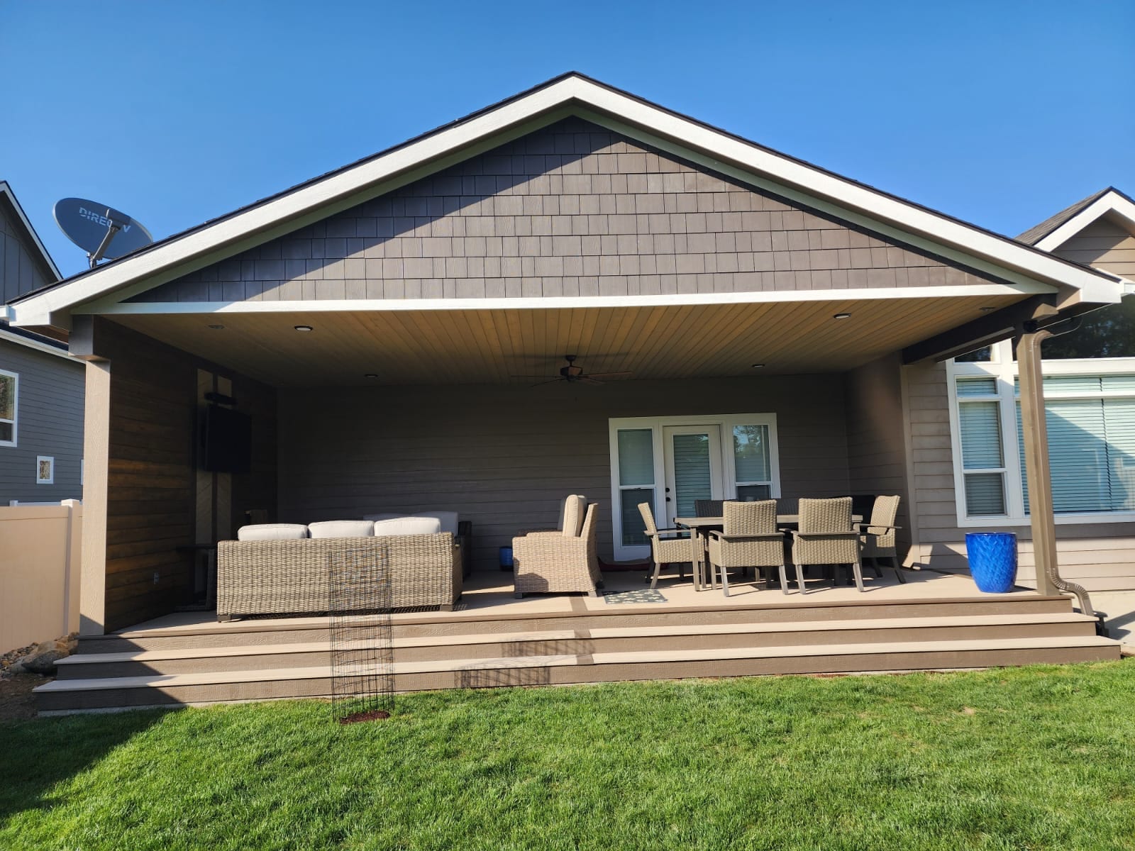Covered backyard deck with gabled roof, wicker furniture, dining set and wide steps down to lawn