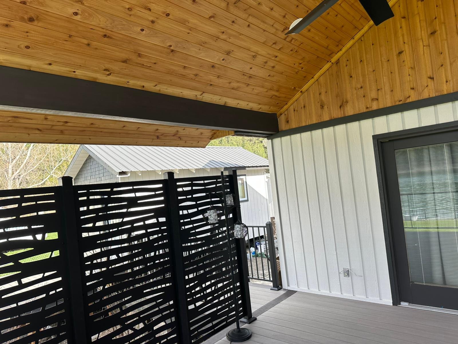 Covered deck with cedar plank vaulted ceiling, ceiling fan, and black slatted privacy screen