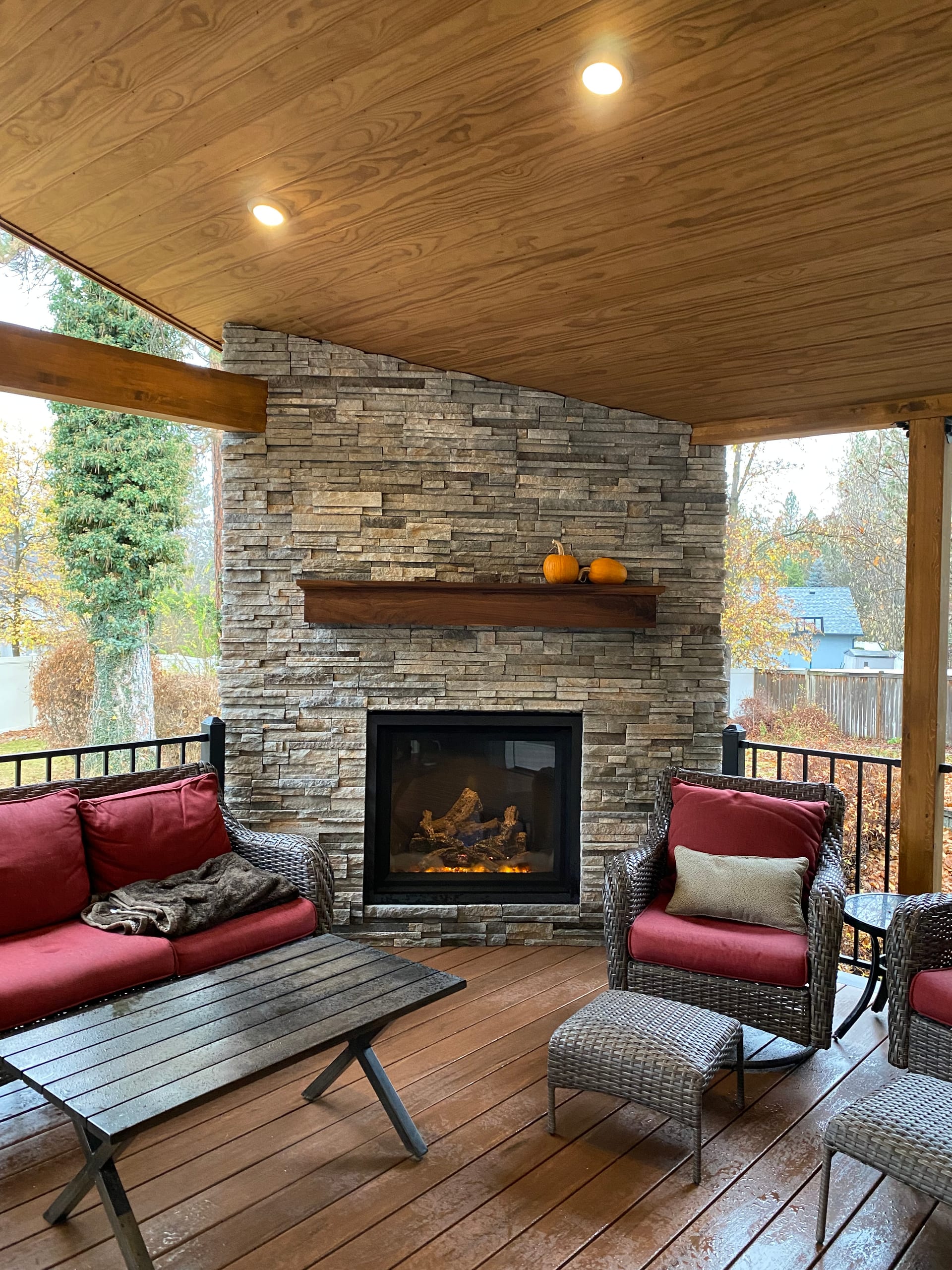 Covered deck with stacked stone fireplace, wood mantel and red-cushioned wicker seating