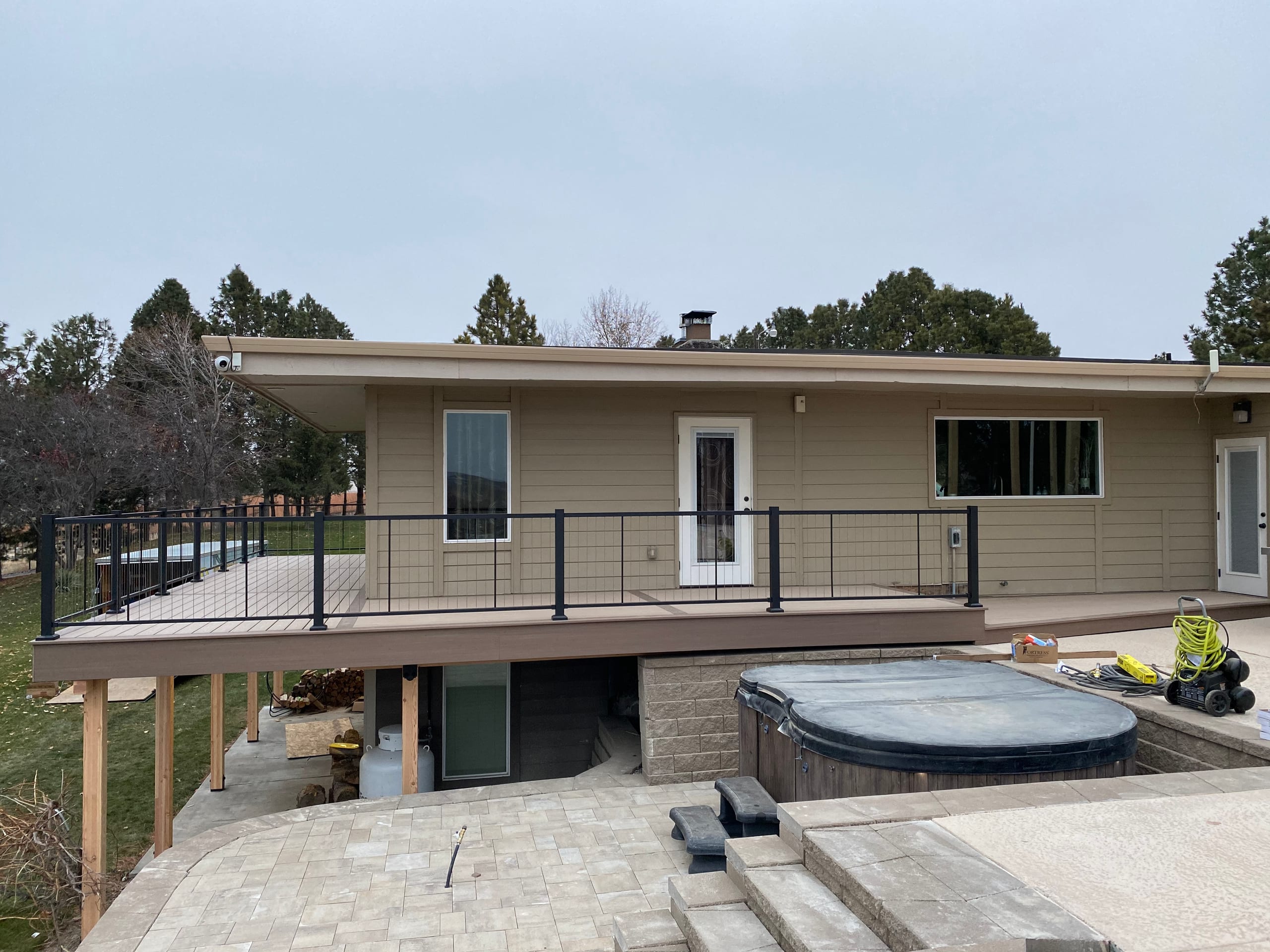 Covered elevated deck with cable railing along a single-story house above a paver patio