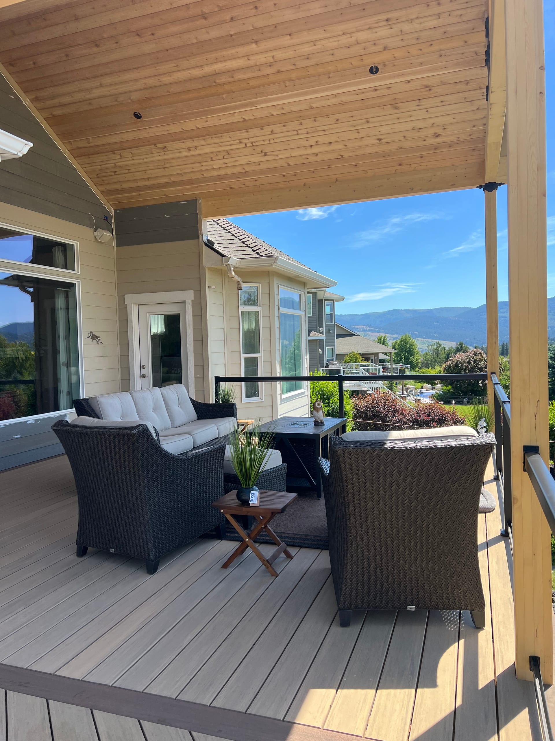 Covered gray composite deck with wicker seating, cedar ceiling and mountain view in warm light
