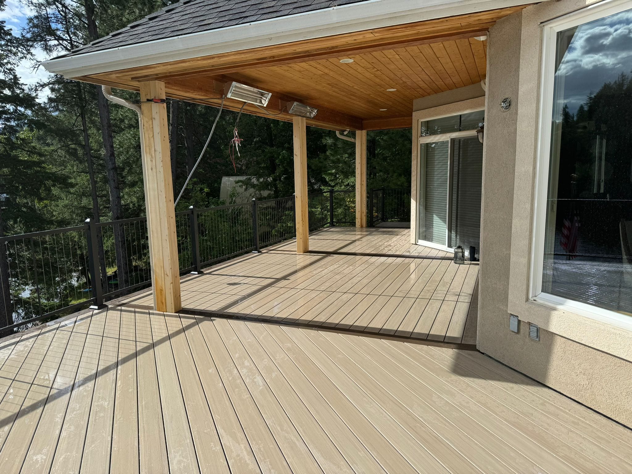 Covered lakeside deck with cedar ceiling, patio heaters, wood posts, tan composite flooring and black railing