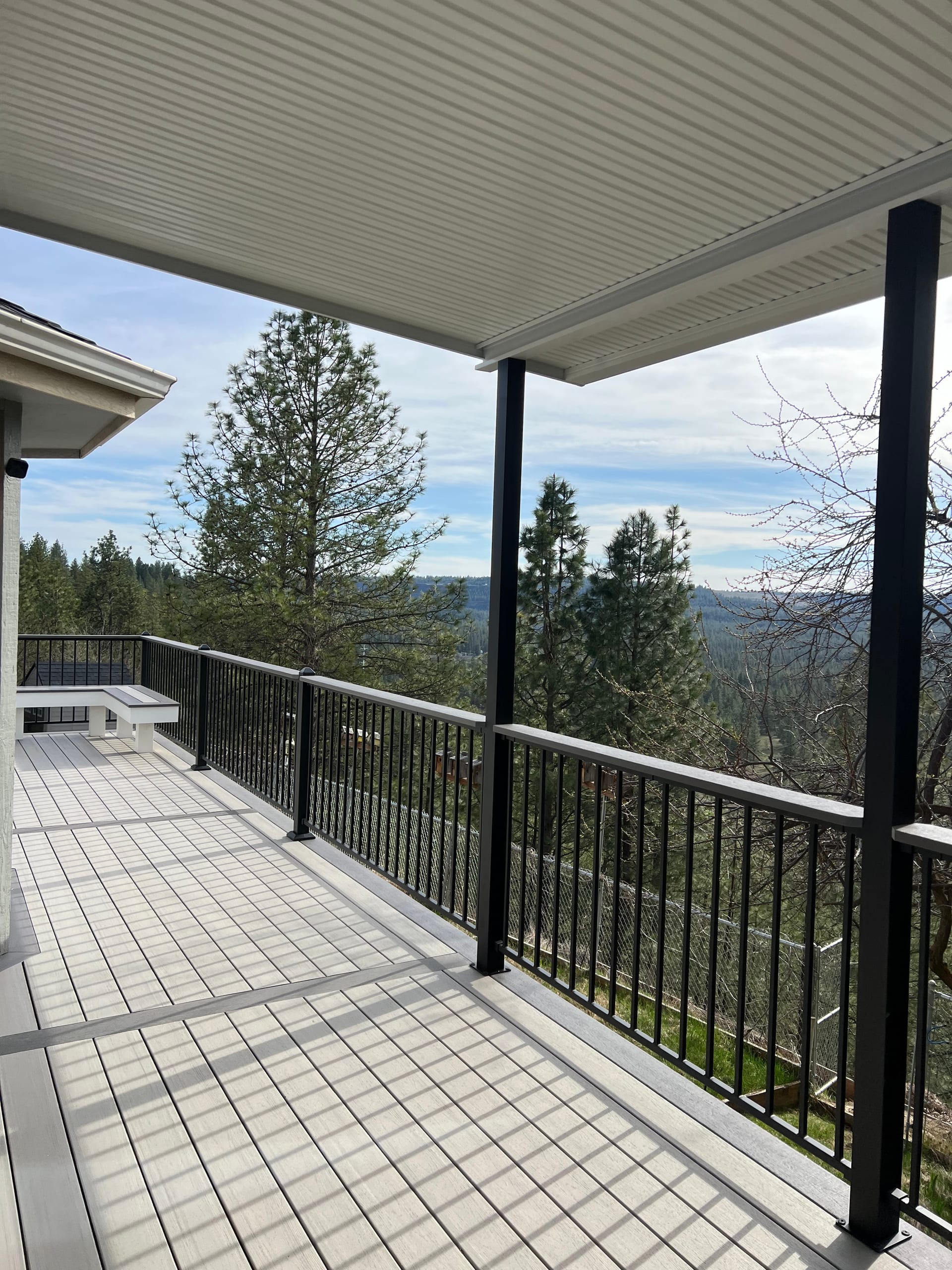 Covered light grey composite deck with black posts and picket railing overlooking forested hills