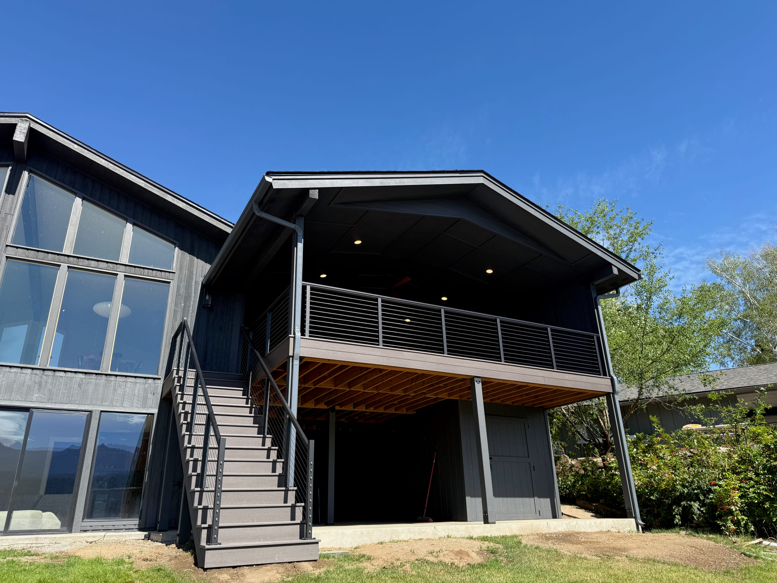 Covered second-story deck with cable railing, gray stairs and recessed ceiling lights on a dark house