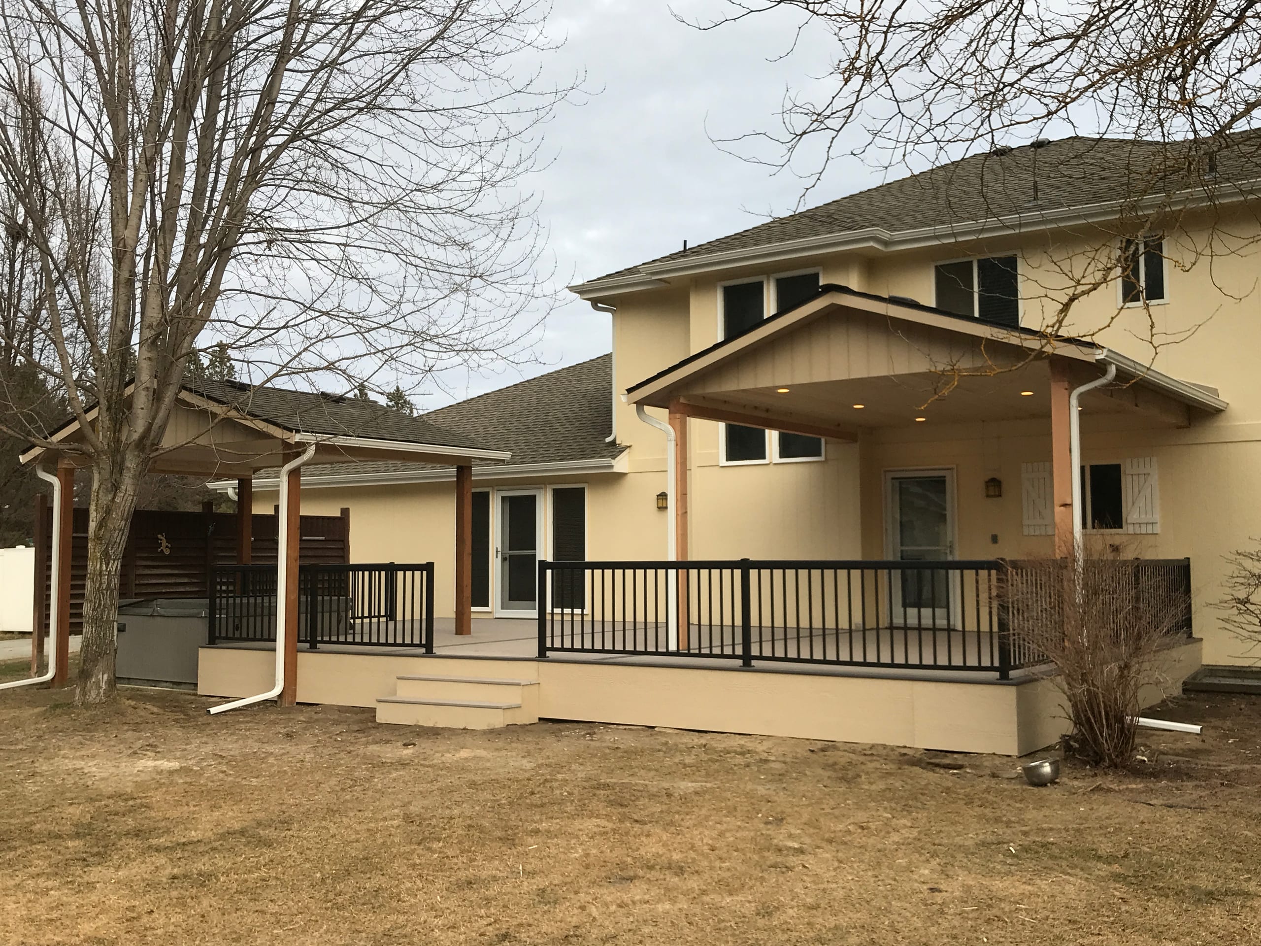 Cream two-story house with gabled covered deck, black picket railing and steps over bare dirt yard