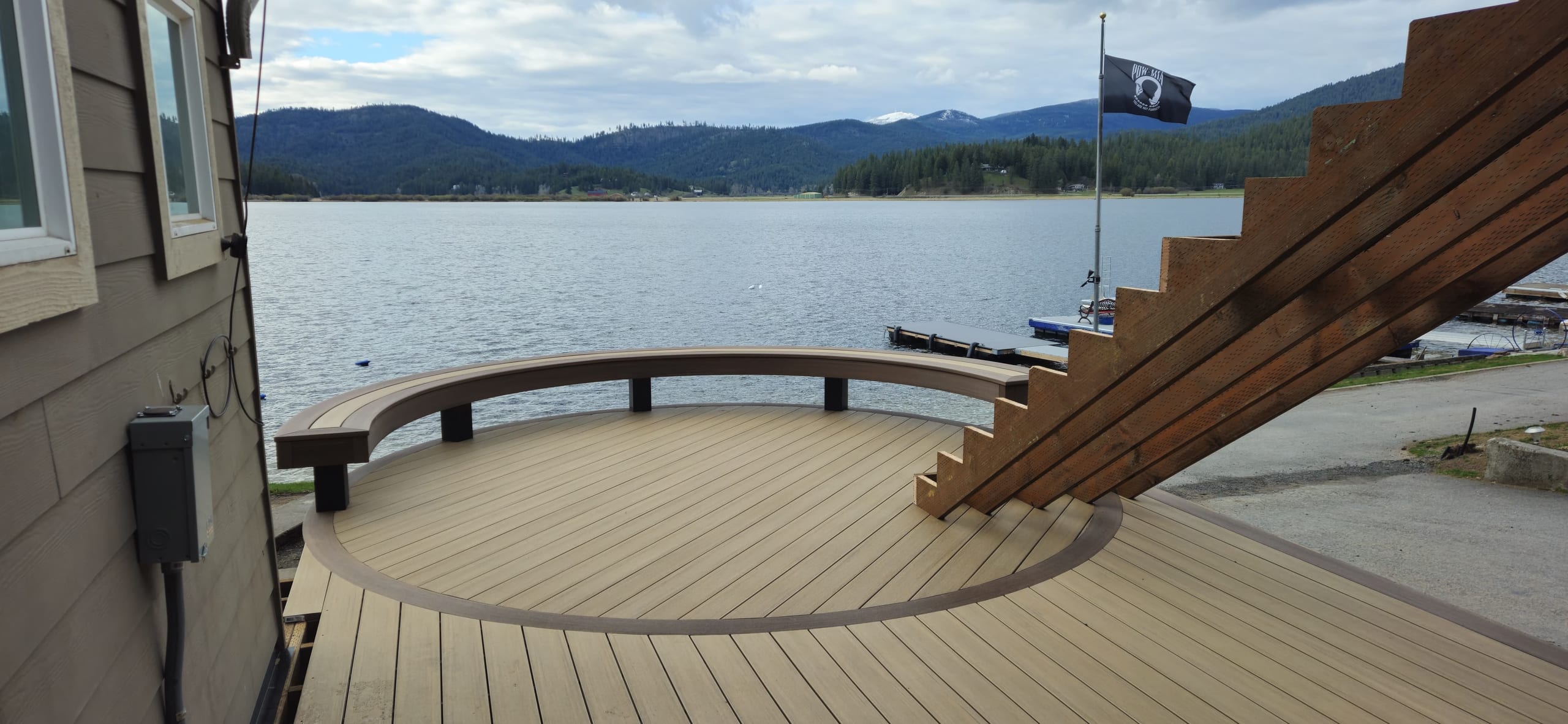 Curved composite deck with bench railing on a lakefront, large wood stair framing and mountains over water