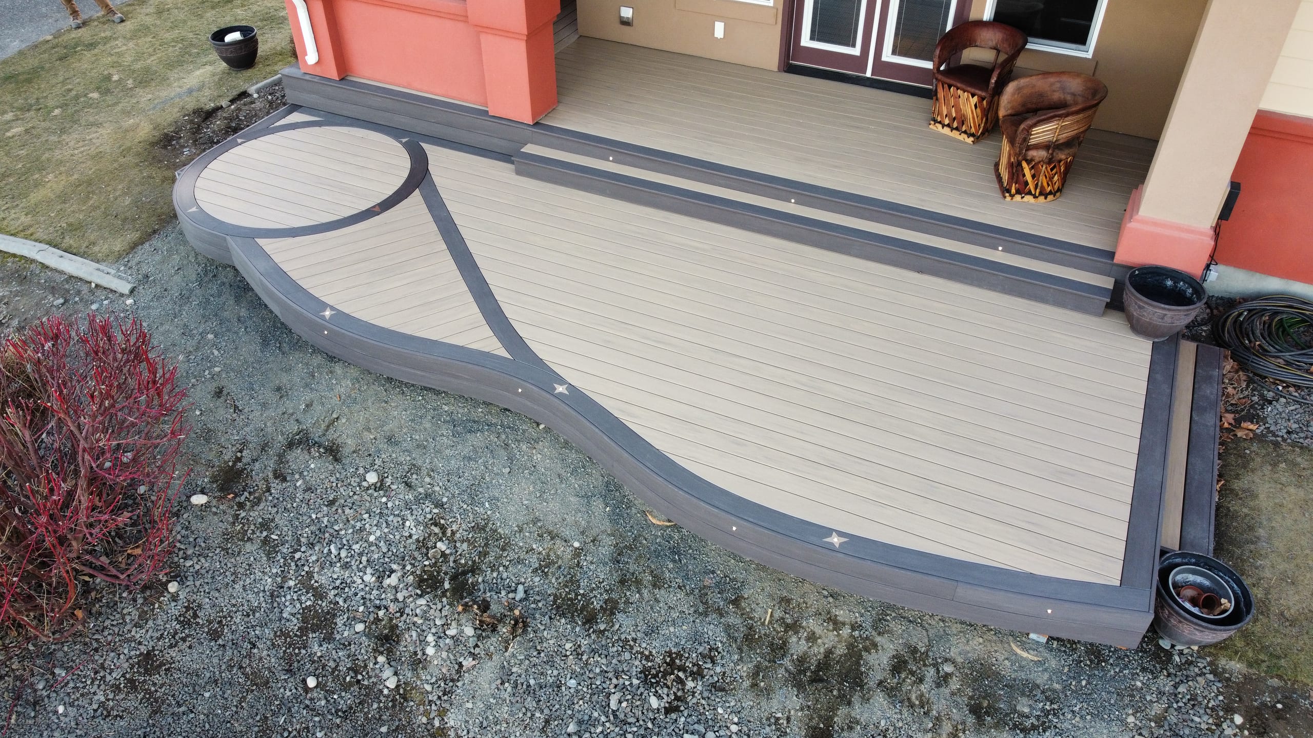 Curved ground-level deck with tan decking, dark border and a circular inlay at a front entry