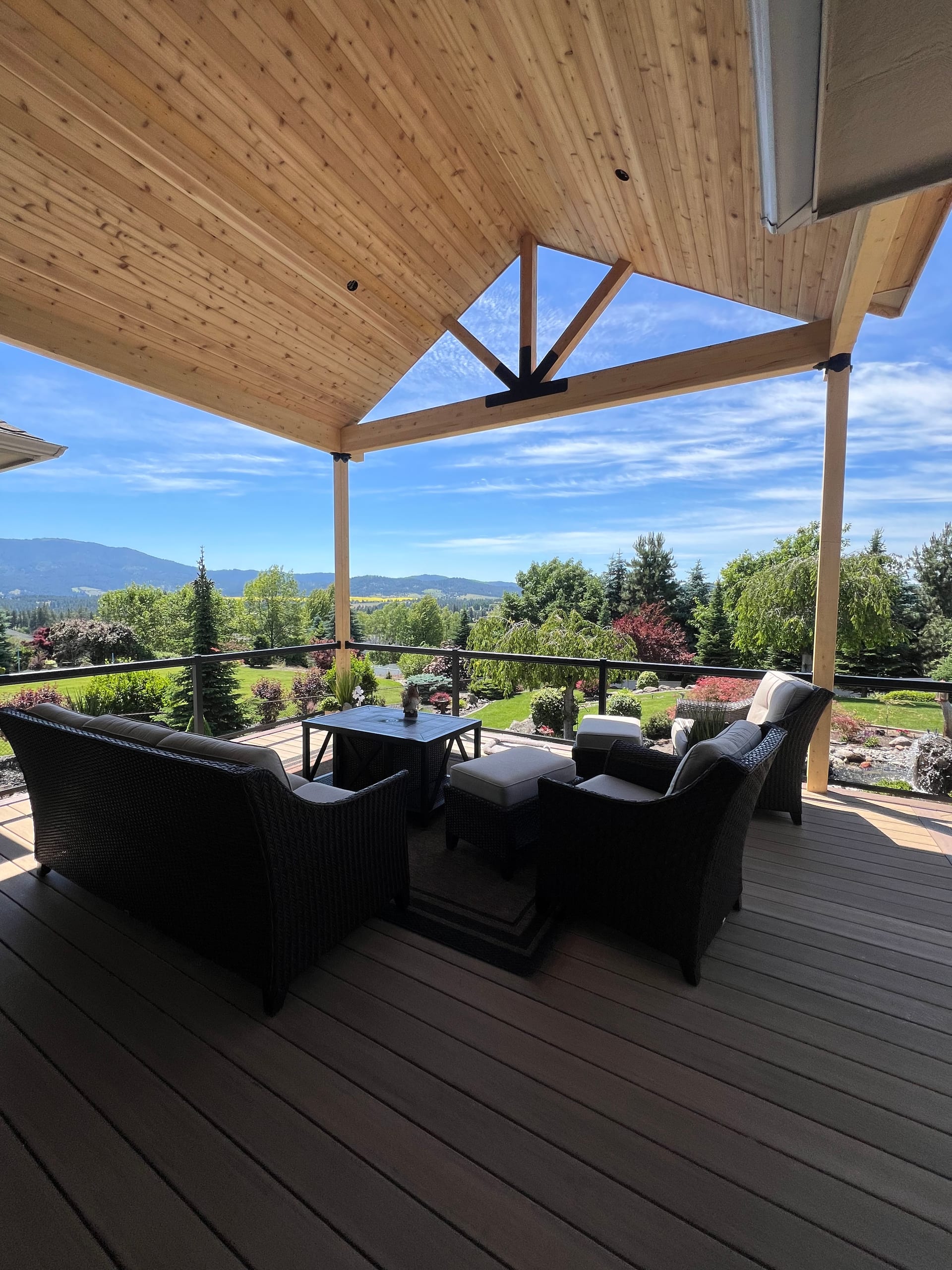 Dark brown composite deck under a cedar-ceiling cover with outdoor sofa seating and a hillside valley view