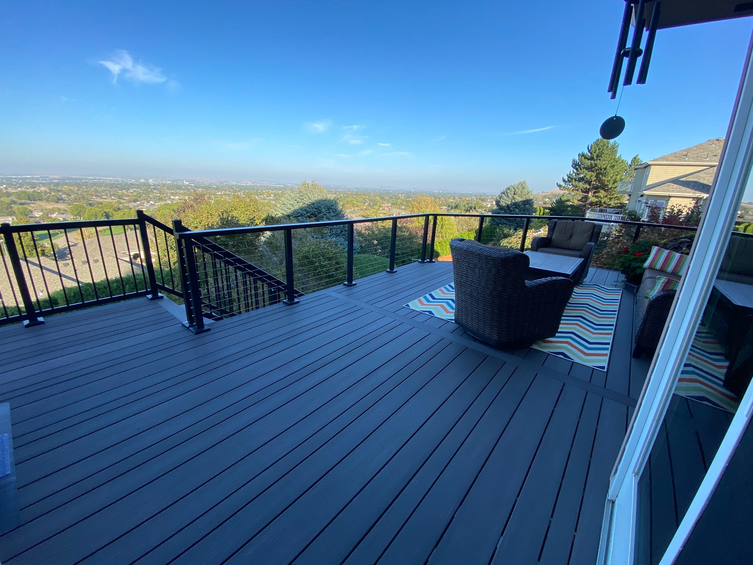 Dark grey composite deck with black cable railing and lounge seating overlooking a valley under blue sky