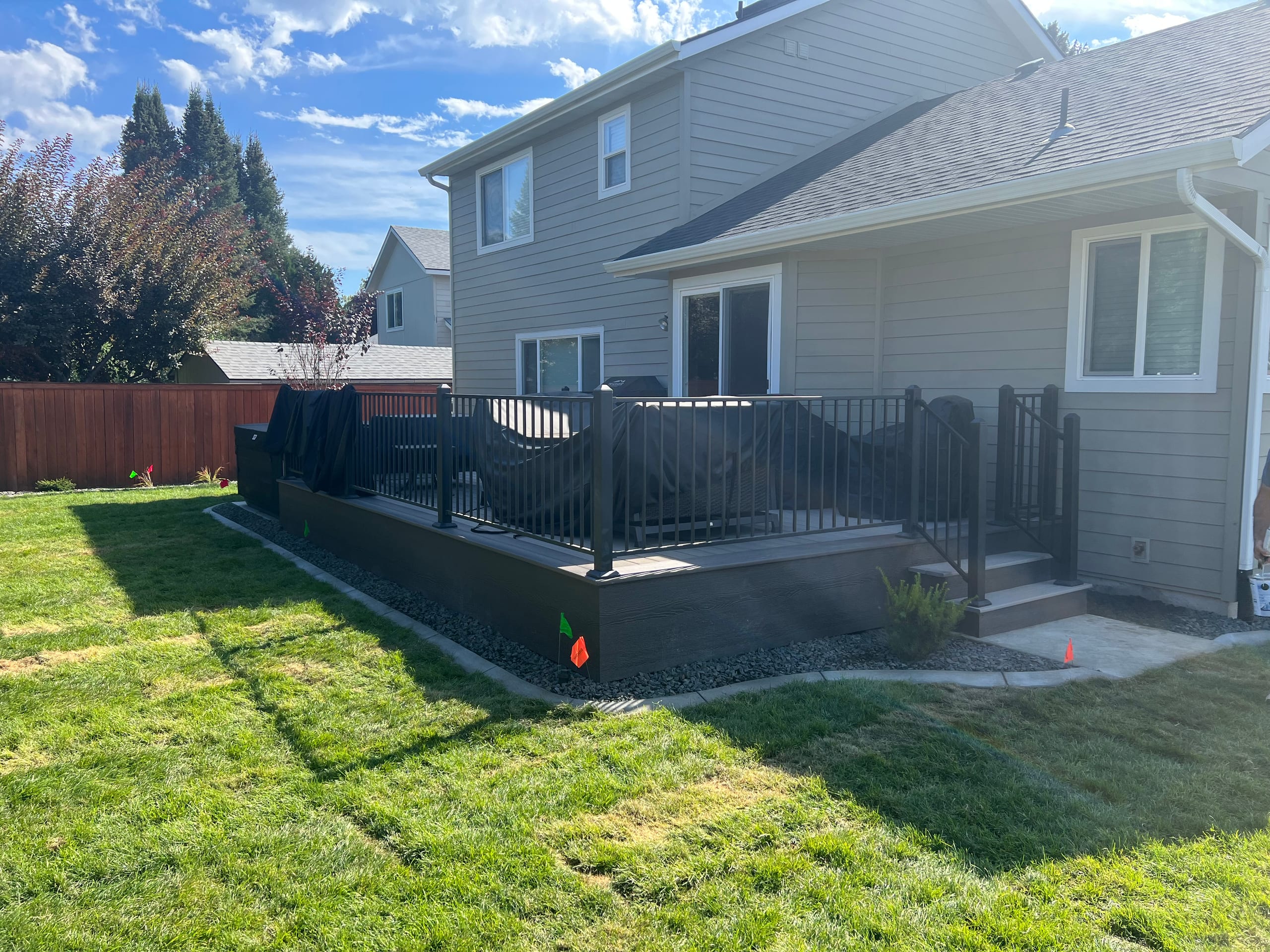 Dark grey composite deck with black railing and steps at a grey house, fresh green lawn