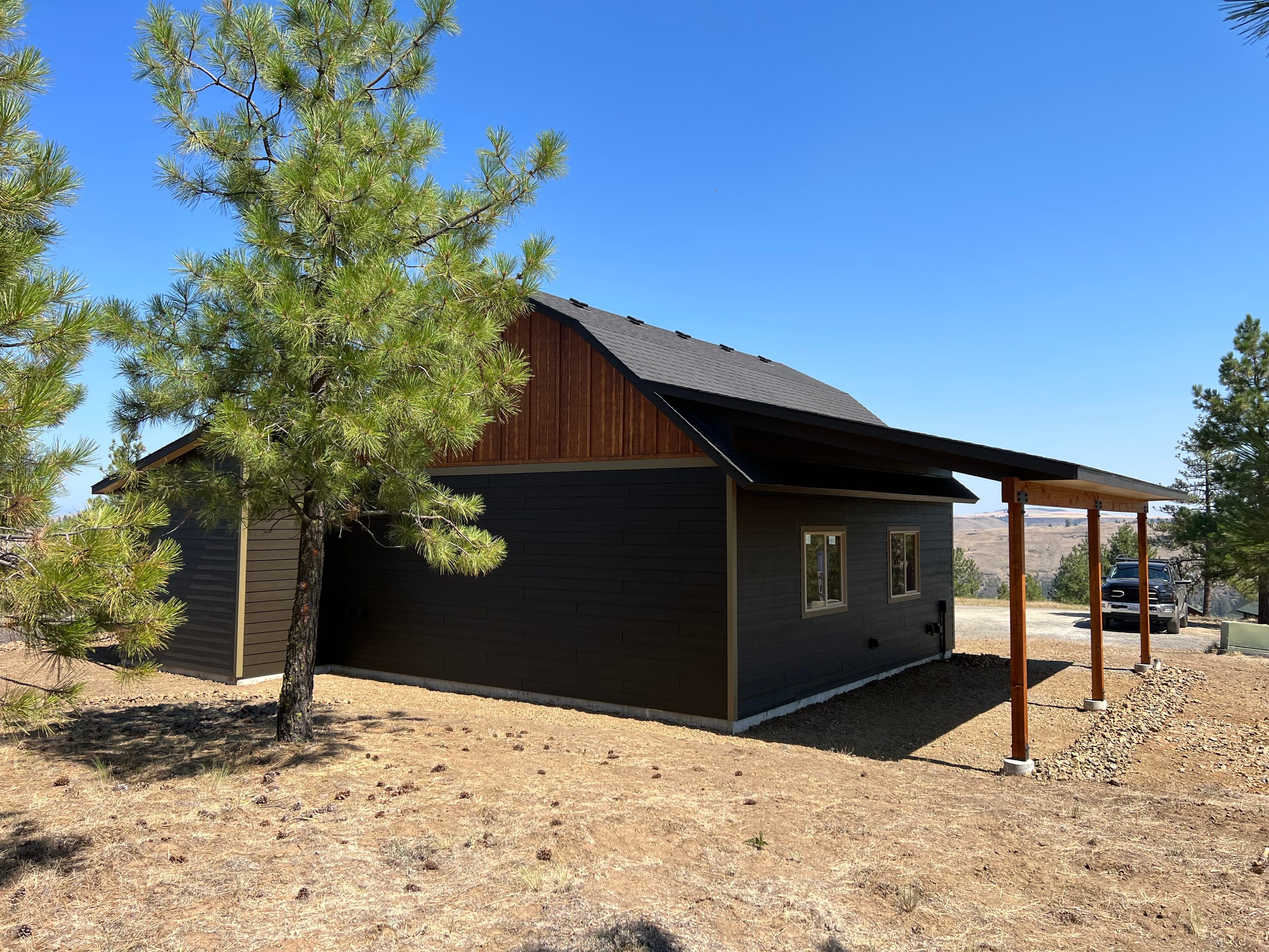 Dark siding barn-style garage with cedar stained gable and covered side carport under blue sky